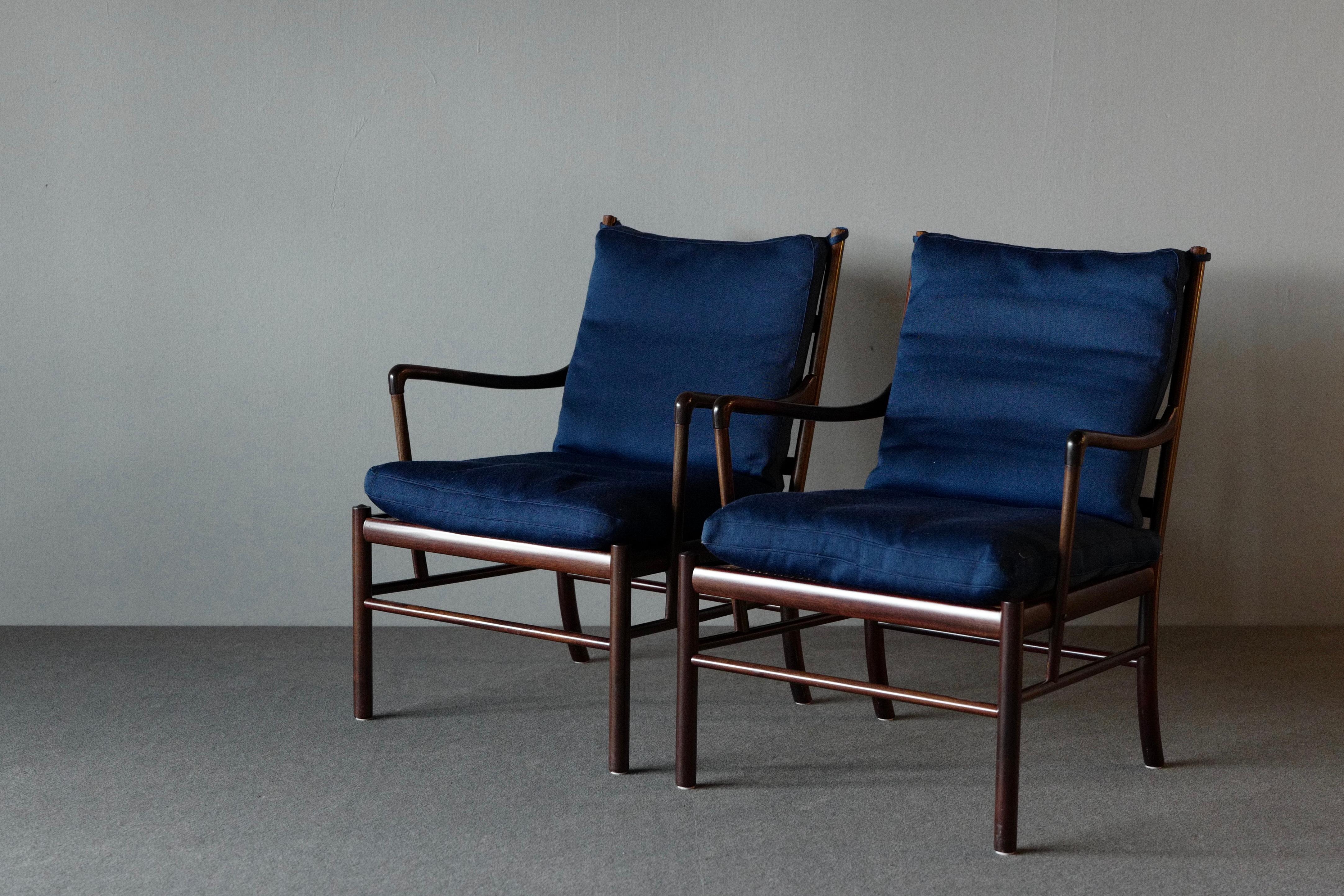 A stunning matching pair of “Colonial” armchairs by Ole Wanscher for P Jepperson. They have a mahogany frame and a woven rattan cane seat. The cushions on the seat and back are upholstered in blue wool. These chairs are elegant and refined in