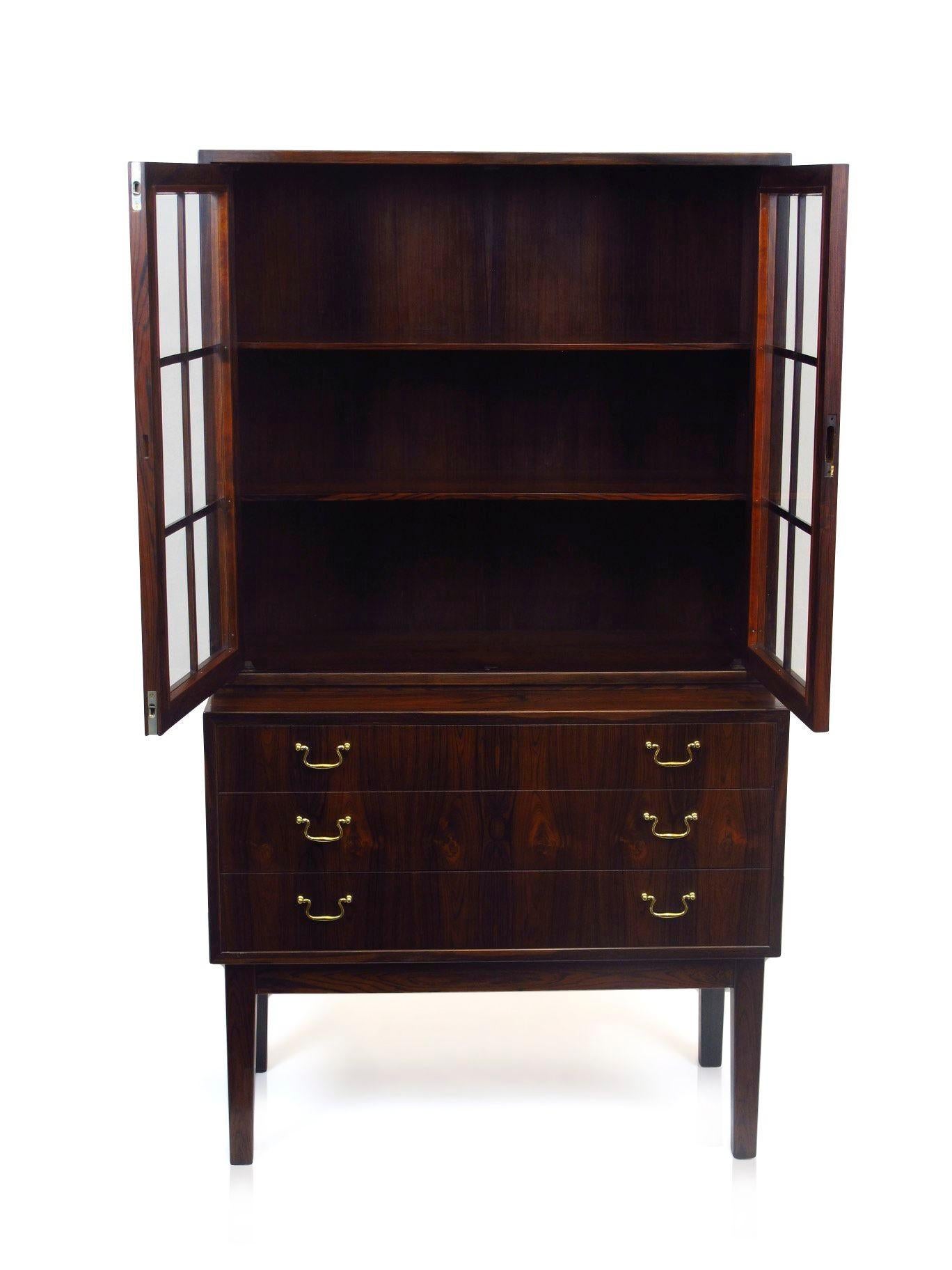 Danish rosewood china cabinet in manner of Ole Wanscher. Features a three-drawer cabinet with brass pulls and locking glass hutch. Dark figured rosewood with pattern match down front of drawers. Glass doors opening to a rosewood lined interior with