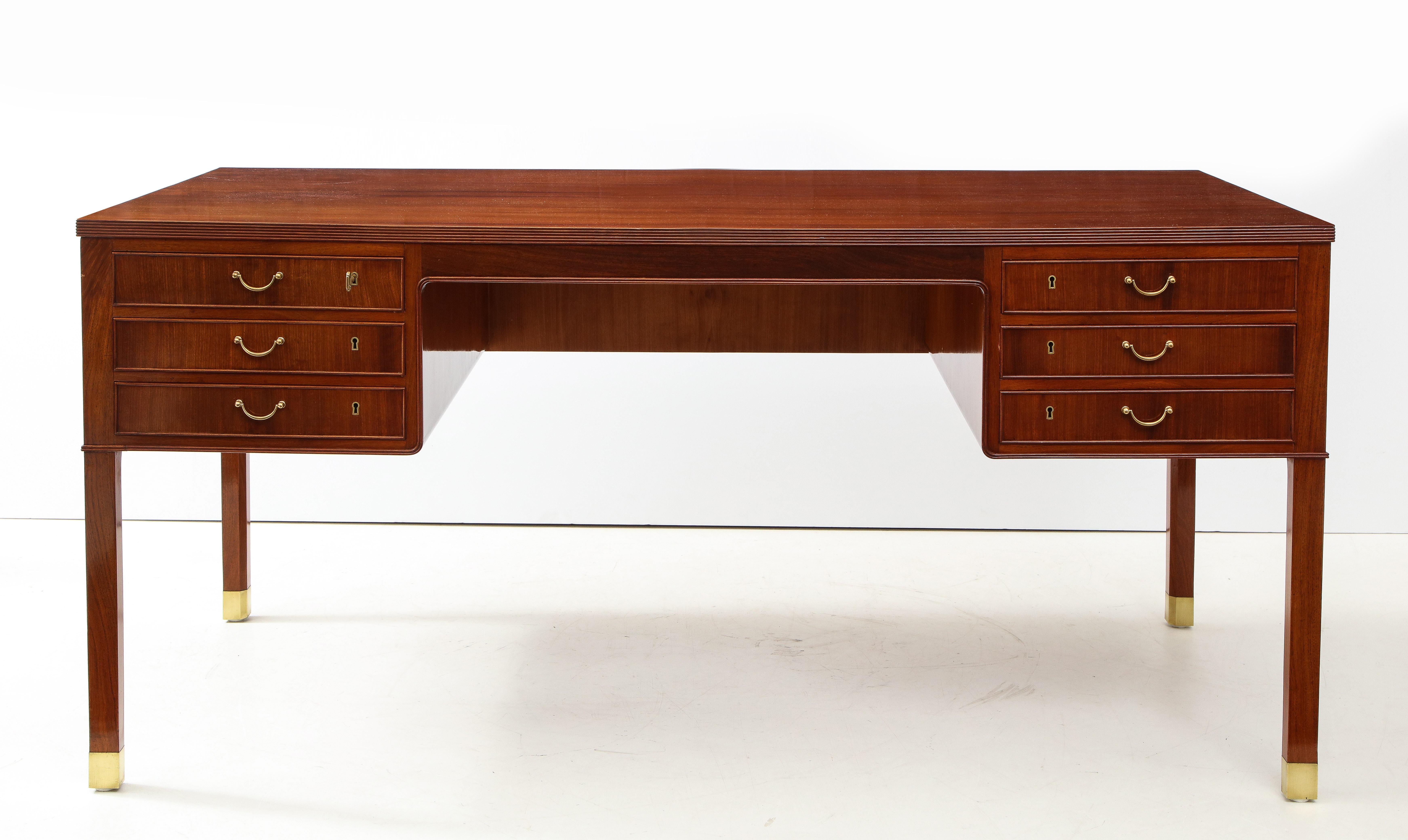 A Danish mahogany and brass-mounted desk designed by Ole Wanscher and produced by A.J. Iversen, circa 1950s. The rectangular top with a reeded edge above six drawers raised on square legs ending with brass caps.