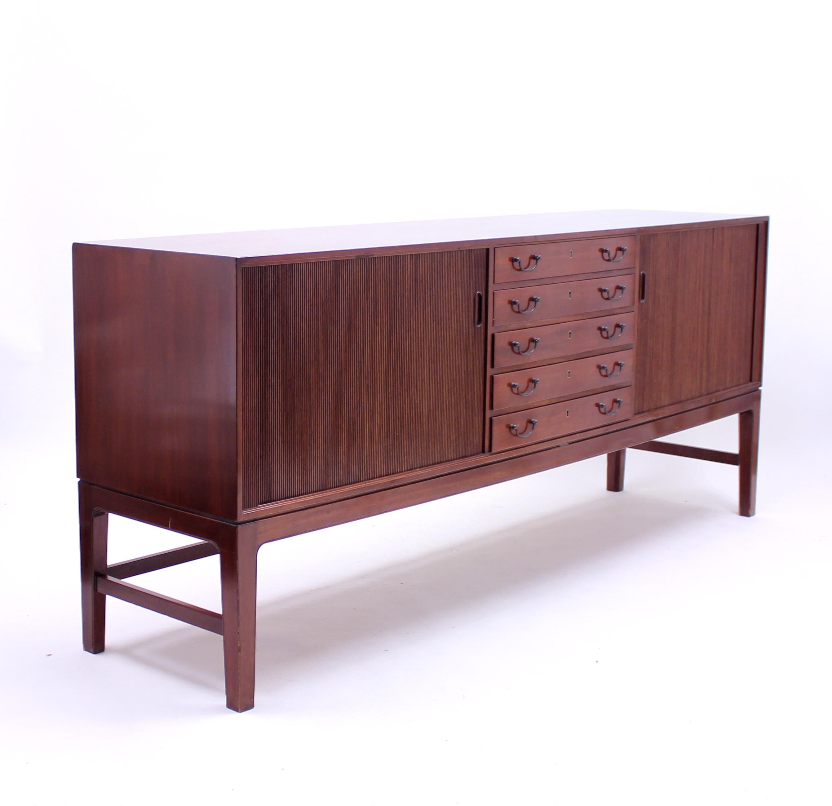 Midcentury mahogany sideboard designed by Ole Wanscher for his longtime collaborator A.J Iversen. Frontside with five drawers and two jalousie doors, one on each side of the drawers. Drawers with removable green felt holders for cutlery and serving