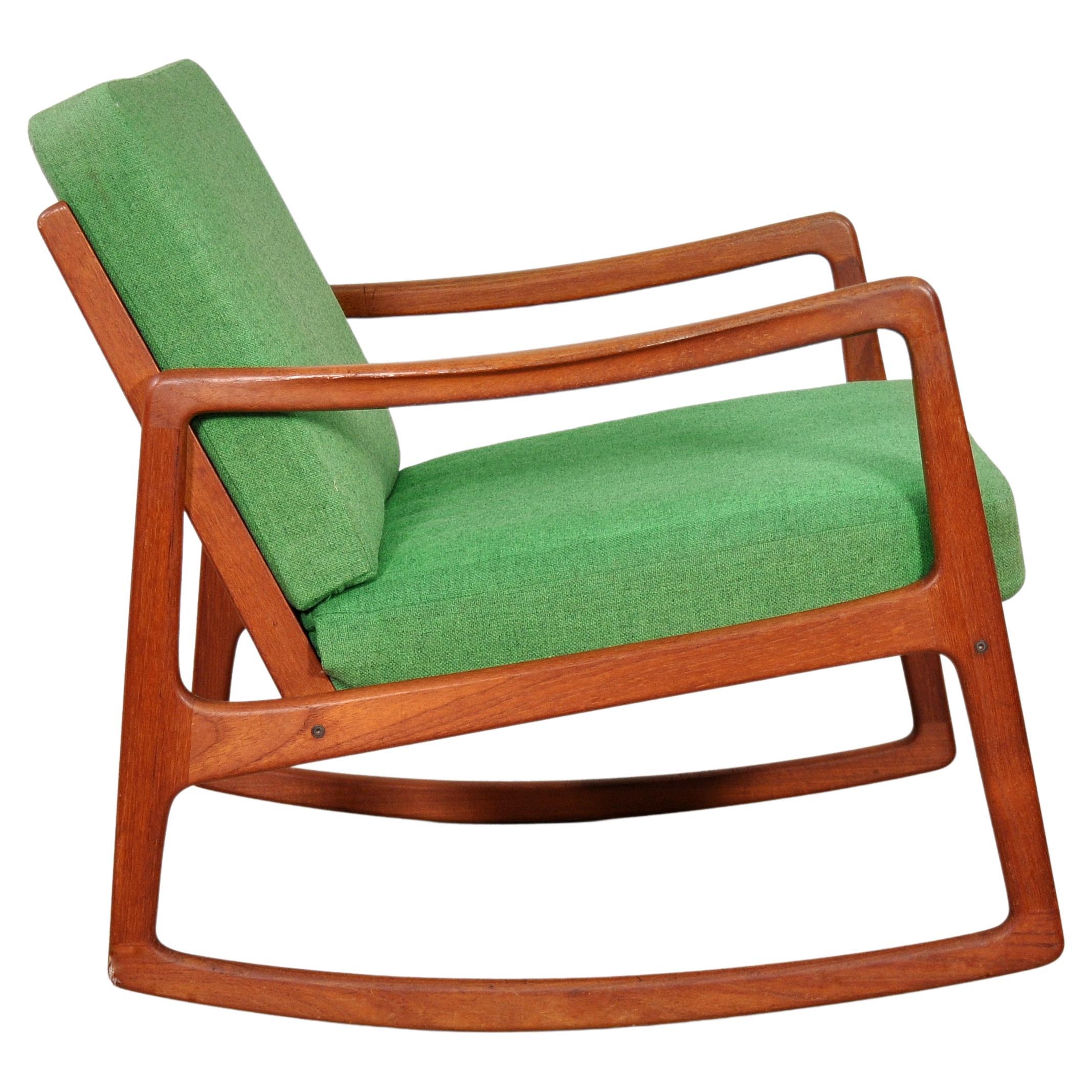 Découvrez l'élégance de ce fauteuil à bascule vintage Eleg 120, au design épuré et minimaliste. Habilement sculpté dans du bois de teck, le rocker présente une finition huilée d'origine avec une belle et riche patine, et les coussins amovibles en