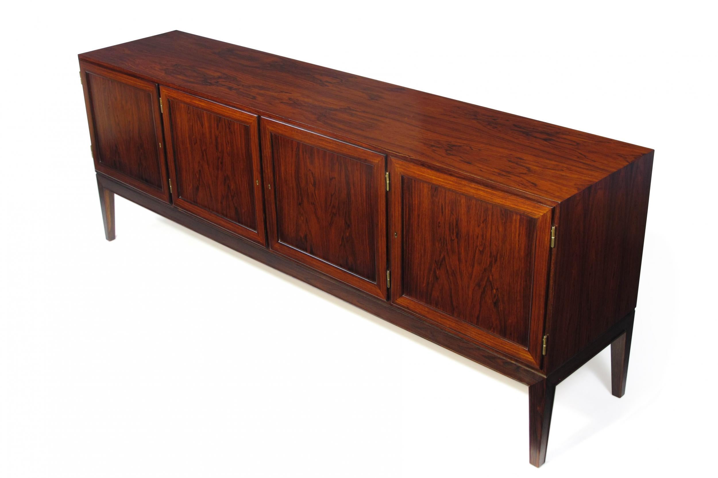 Finely crafted credenza of dark rosewood with pattern match across the front of doors attributed Ole Wanscher. Fully locking doors open to reveal a mahogany interior with an adjustable shelf and series of silverware drawers on the left side. Raised