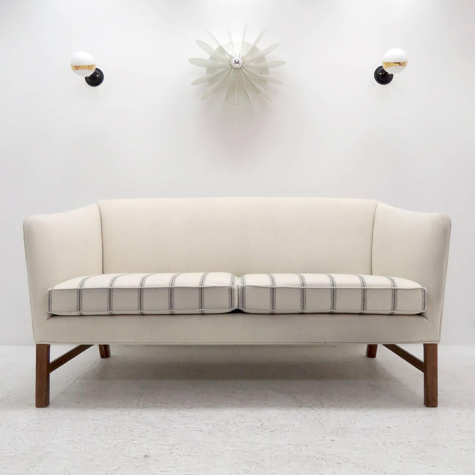 Wonderful settee designed by Ole Wanscher, produced by A.J. Iversen, Denmark in 1960 with eggshell colored wool fabric and lightly striped seat cushion on Cuban mahogany legs.