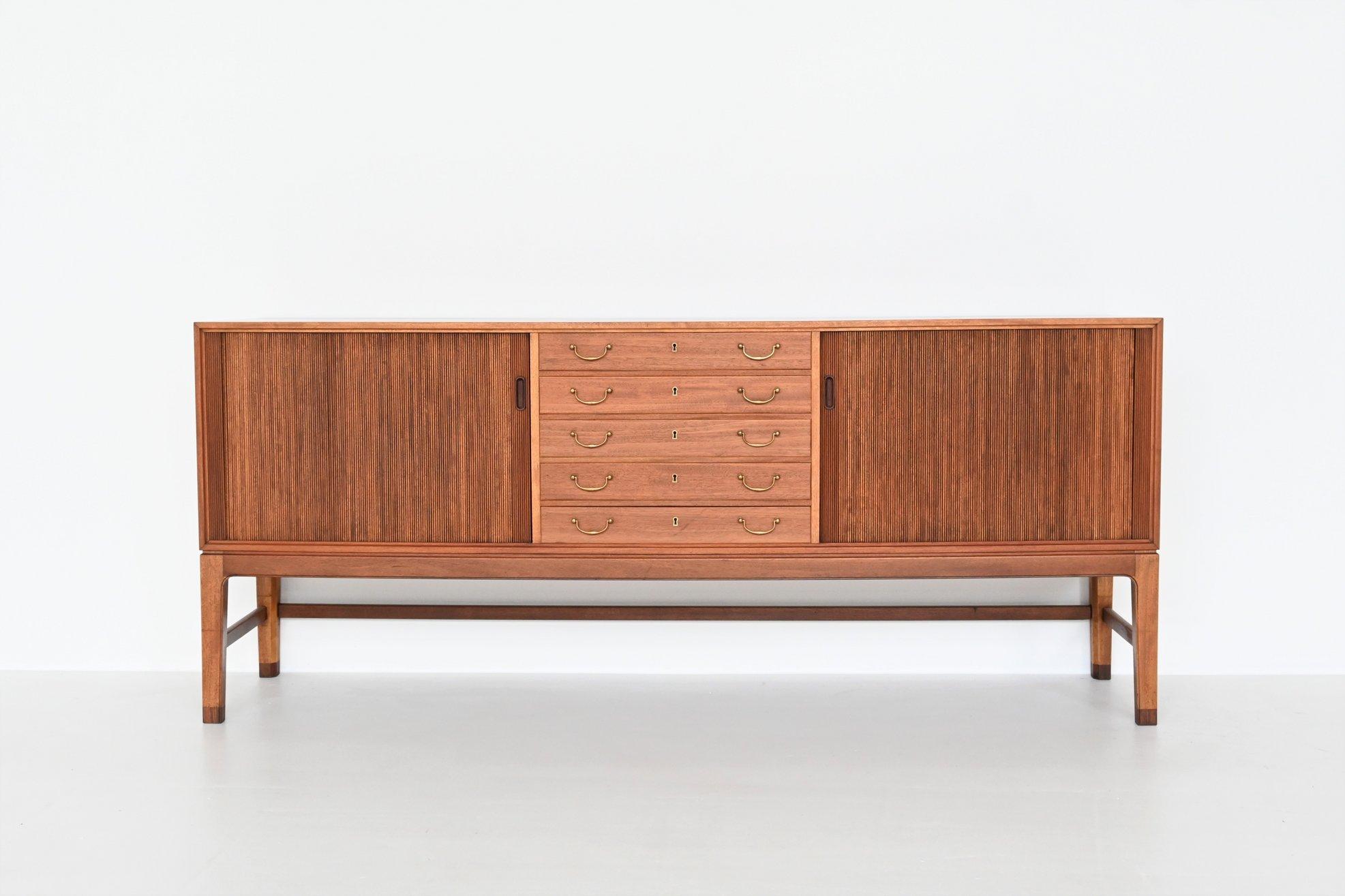 Beautiful elegant sideboard designed by Ole Wanscher and manufactured by A.J. Iversen, Denmark 1940. This well-crafted sideboard features five centered drawers with brass handles and tambour doors on either side hiding shelves inside. The lines of
