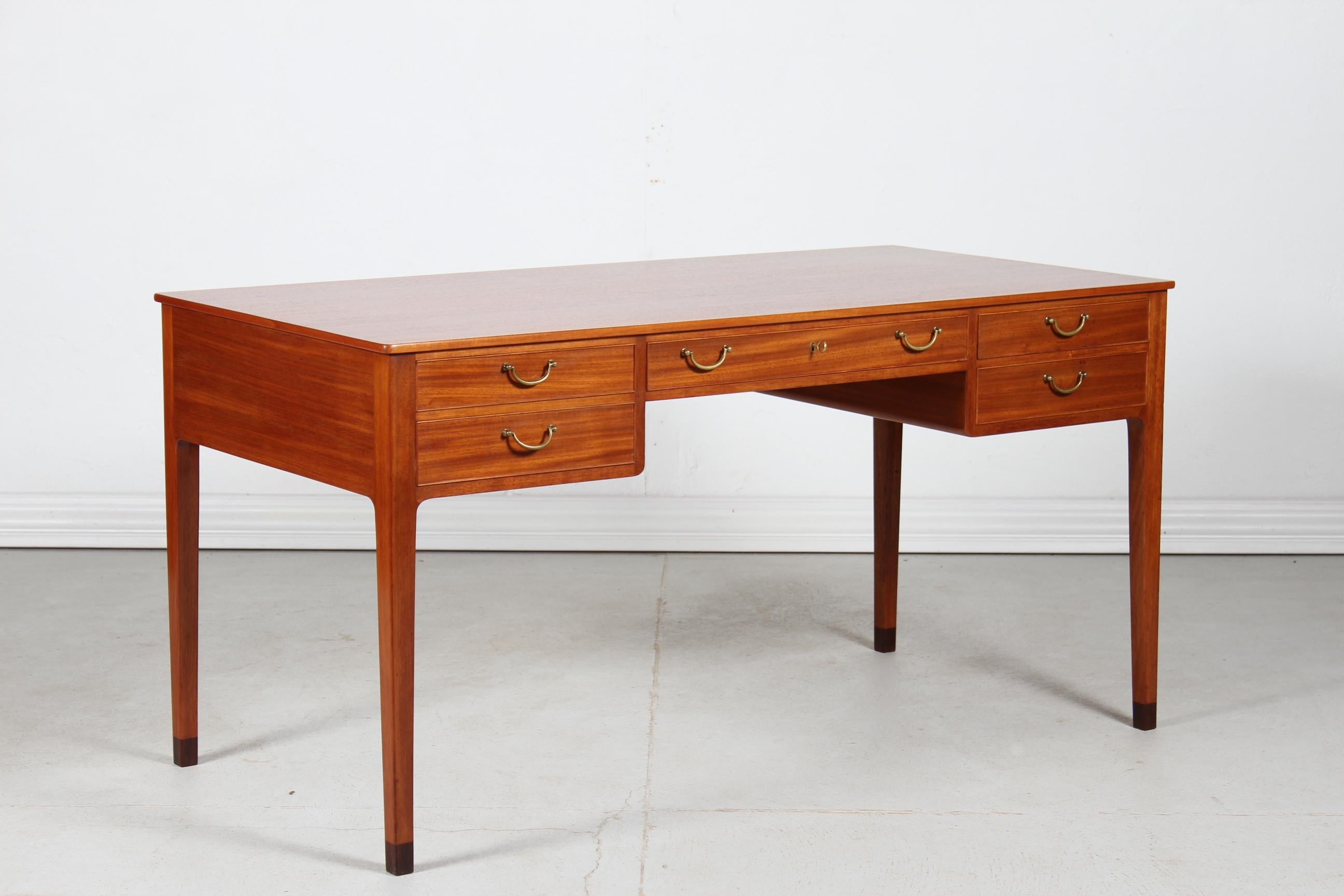 Free standing writing desk with 5 drawers designed by Ole Wanscher (1903-1985).
The desk is made of lacquered mahogany with inside frame of oak. 
The handles are made of solid brass and the original leg ends are mounted with dark wood.

It's
