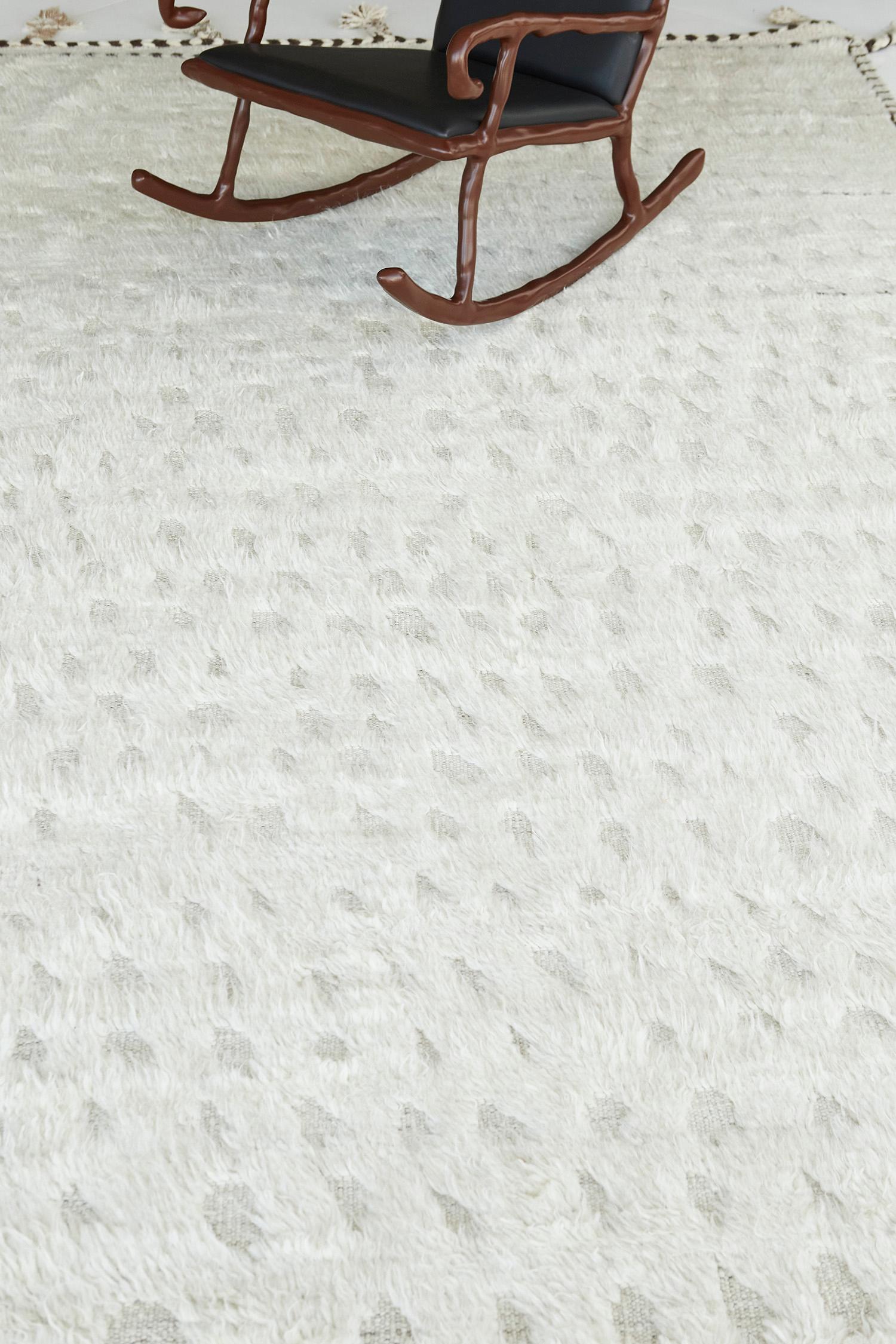 Olea' est un tapis à poils longs en laine nouée à la main, construit sur une base à tissage plat. Les détails des pompons courent le long des côtés avec des marques de points foncés. Cette pièce ludique a une base parfaitement blanche avec des