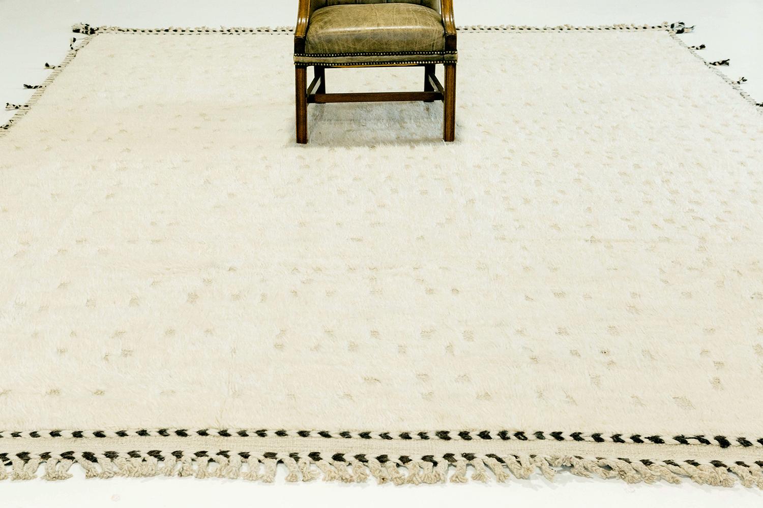 Olea' is a hand knotted wool shag rug built on a flat-weave base. Tassel detailing run along the sides with dark stitch marks. This playful piece has a perfectly white foundation with round embossed details filling in the space and playing with the