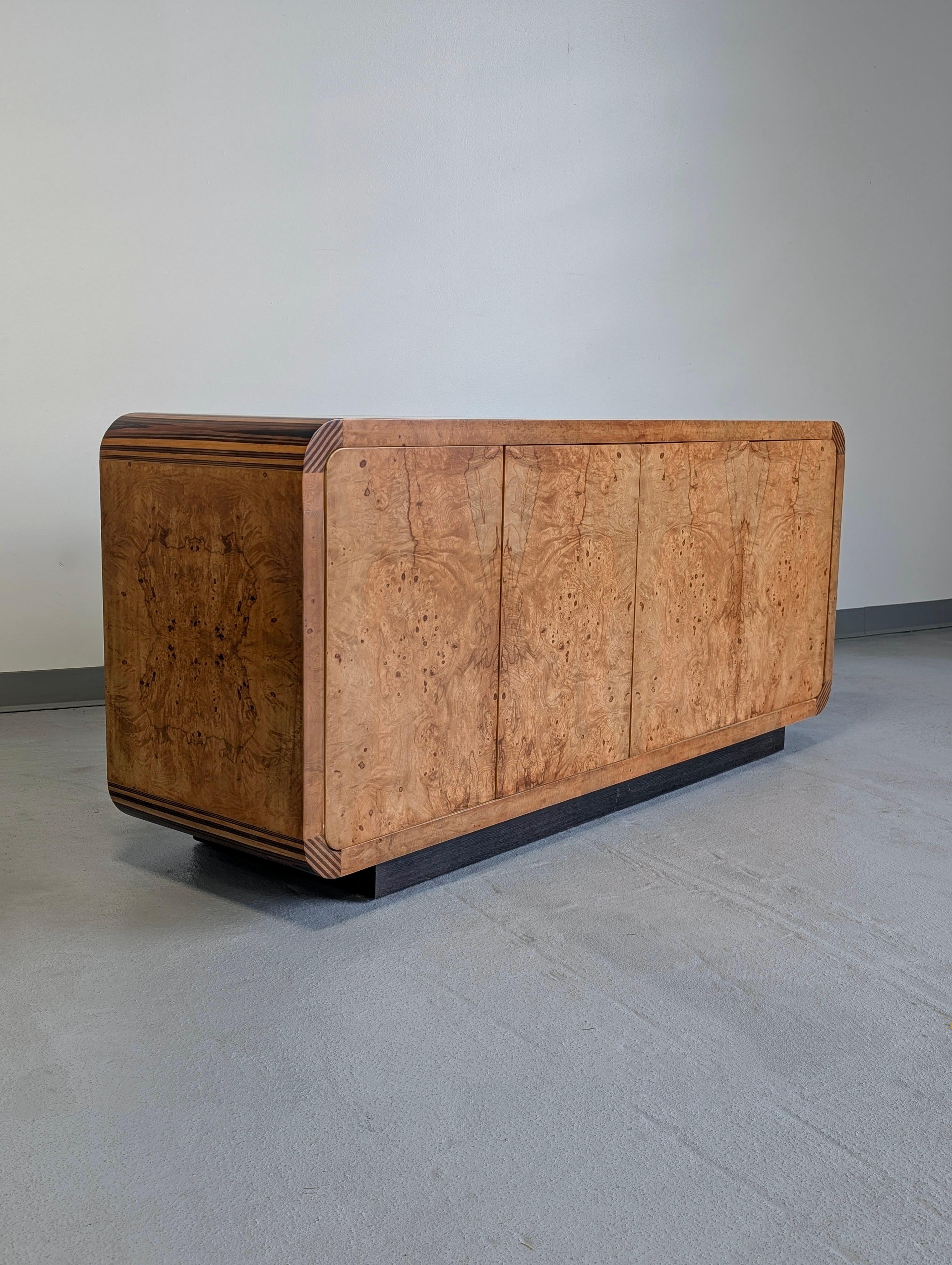 Henredon scene two credenza sideboard buffet cabinet in olive ash burl bookmatched veneer with zebra wood corners and four flush doors with spring clip closures. Divided into two compartments each with a single drawer and adjustable shelf. One