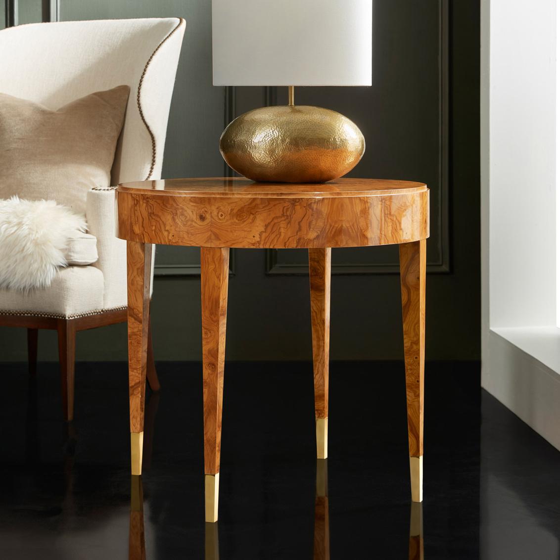 The table's circular top and clean-lined silhouette create a modern canvas that allows the wood's stunning natural patterns to take center stage. 

The elegant design is supported by four gracefully tapered legs, each finished with refined brass