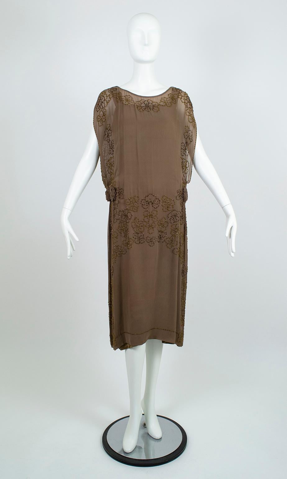 Provenant de la succession de l'héritière des grands magasins Estela Jácome, cette robe exceptionnelle du début des années 20 est l'exemple même d'une modestie séduisante. Malgré ses rosettes sensuelles au niveau des hanches, ses côtés tabard très