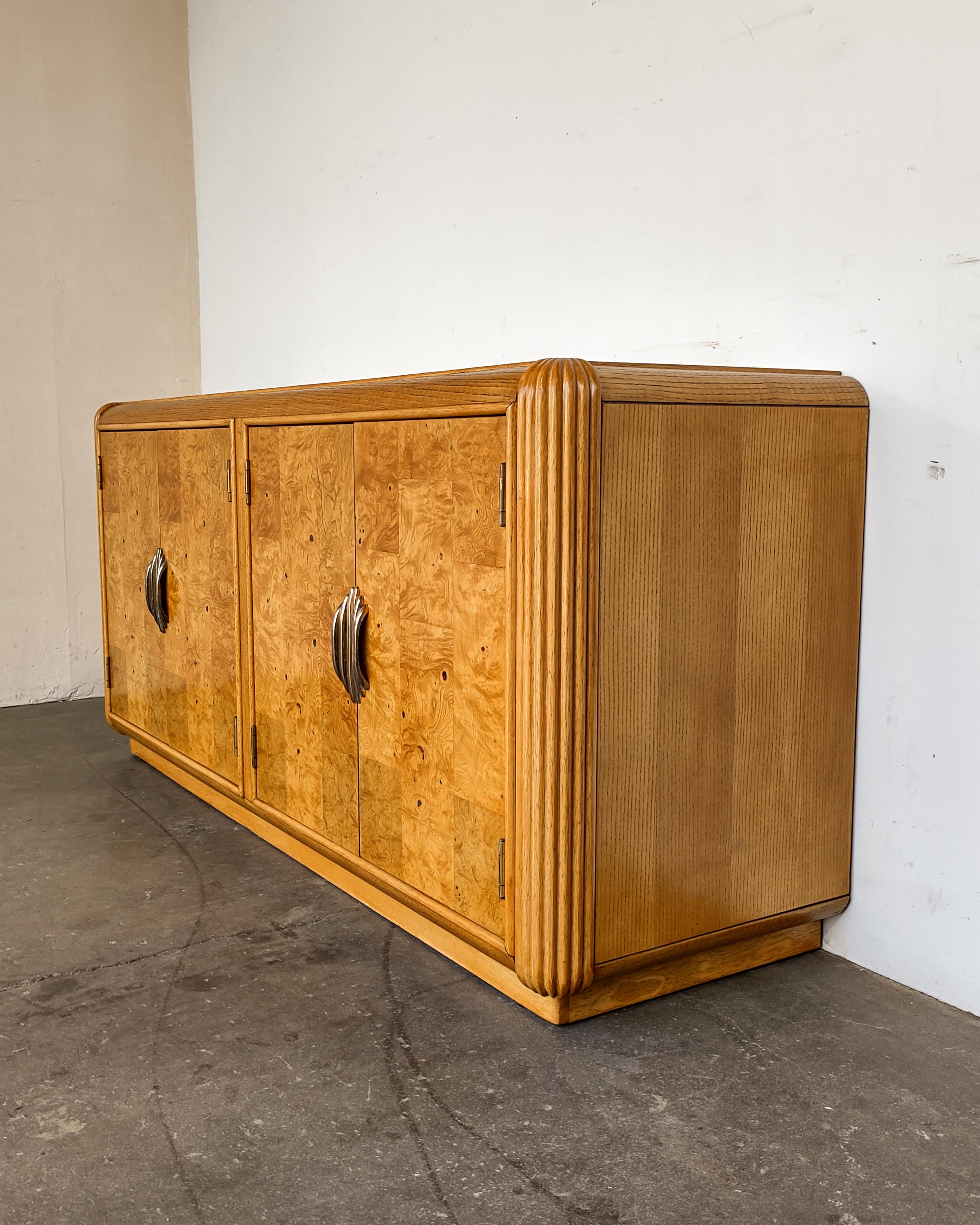 Art Deco revival burl wood and oak credenza circa 1980s. Completely refinished to show beautiful wood grain, rounded fluted corners and patchwork burl doors. Unique original patinaed brass pulls. Interior features drawer and removable shelf on each