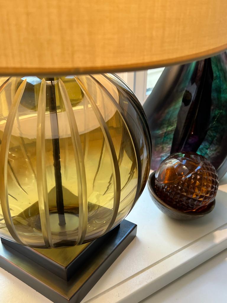 The mouth blown and hand carved striking olive color glass is about 30 cm ( 1 foot ) in diameter and becomes a focal point in any interior. The cast metal base, woven electric cord and the fabric shade, all add to its timeless character.
The lamp