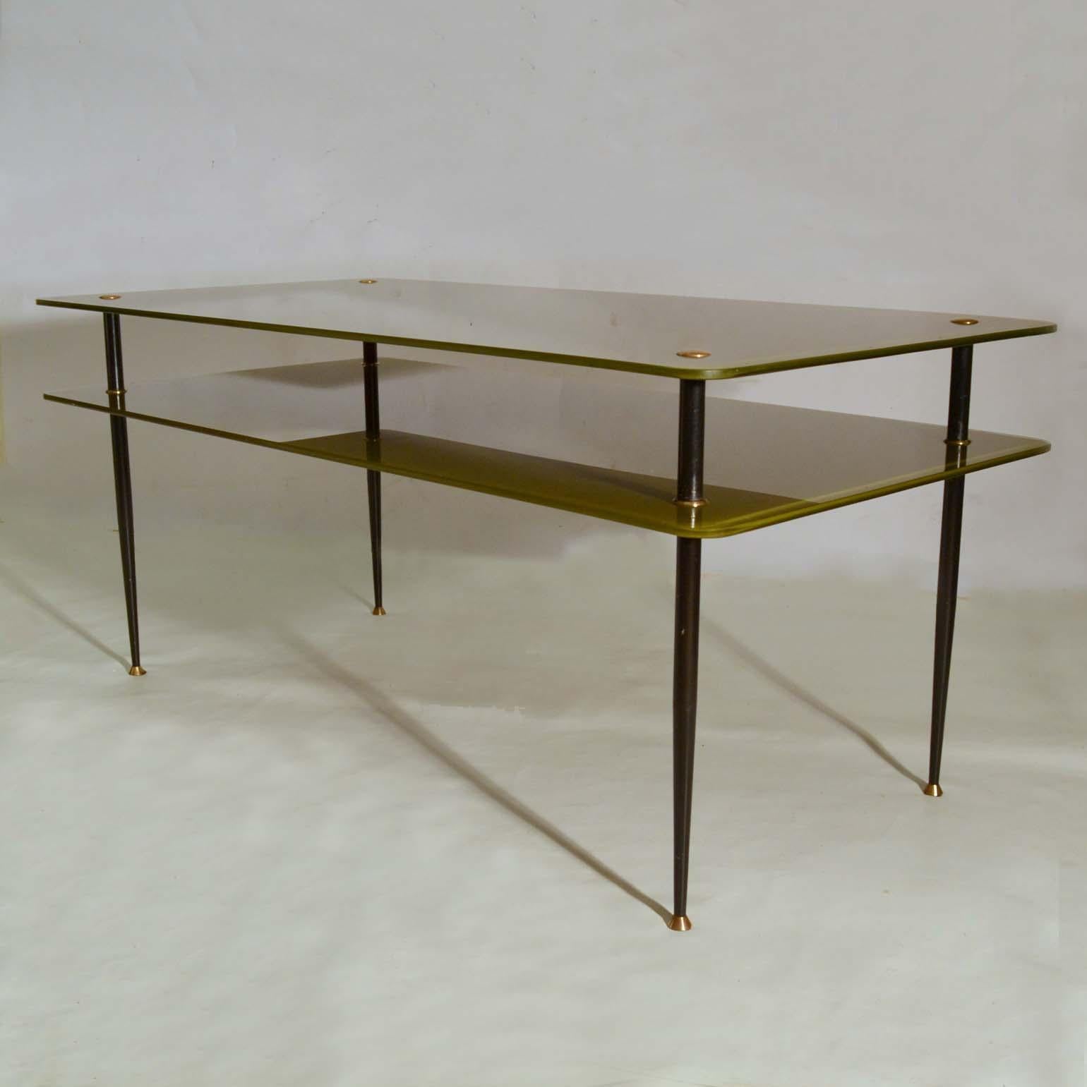 Olive green double layered tempered and painted glass coffee table connected by four black lacquered metal tapered legs. They are highlighted by brass fittings connecting the legs and feet. This unusual colored table distinguishes itself by applying