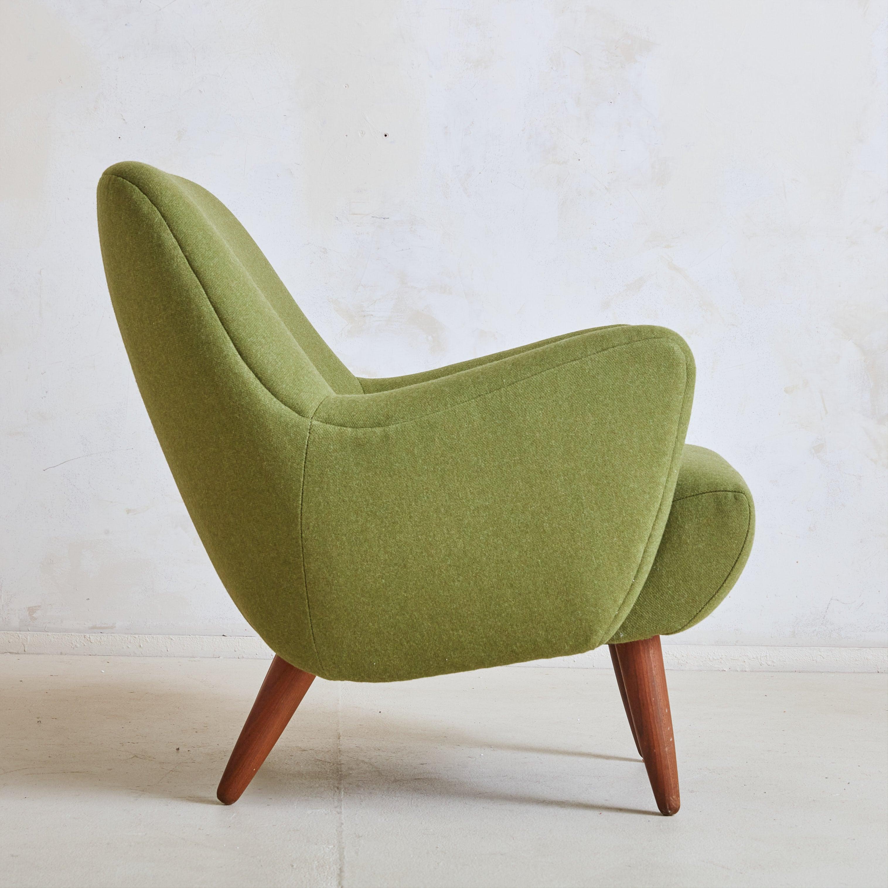 A 1950s Danish Modern armchair newly reupholstered in striking olive green fabric. The sculptural silhouette features a softly curved back and exaggerated boomerang arms. This low-profile chair stands on four tapered wooden legs in a rich, brown