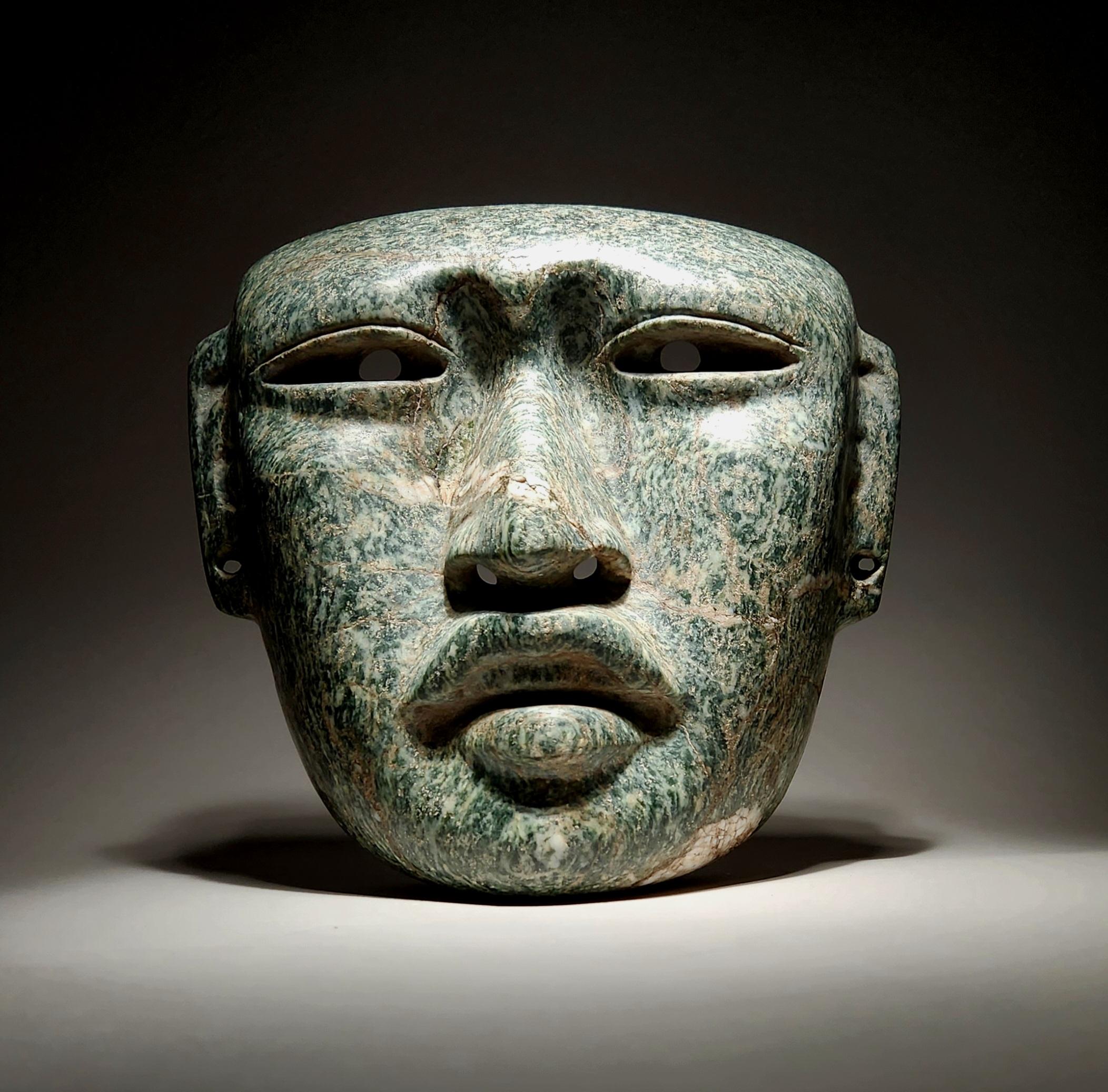 A large and powerful portrait mask depicting an important Olmec ruler, with a broad face, furrowed brow, rectangular ear flanges, full lips, and a large nose, carved from a variegated green stone with white quartz inclusions, Olmec Culture, Gulf