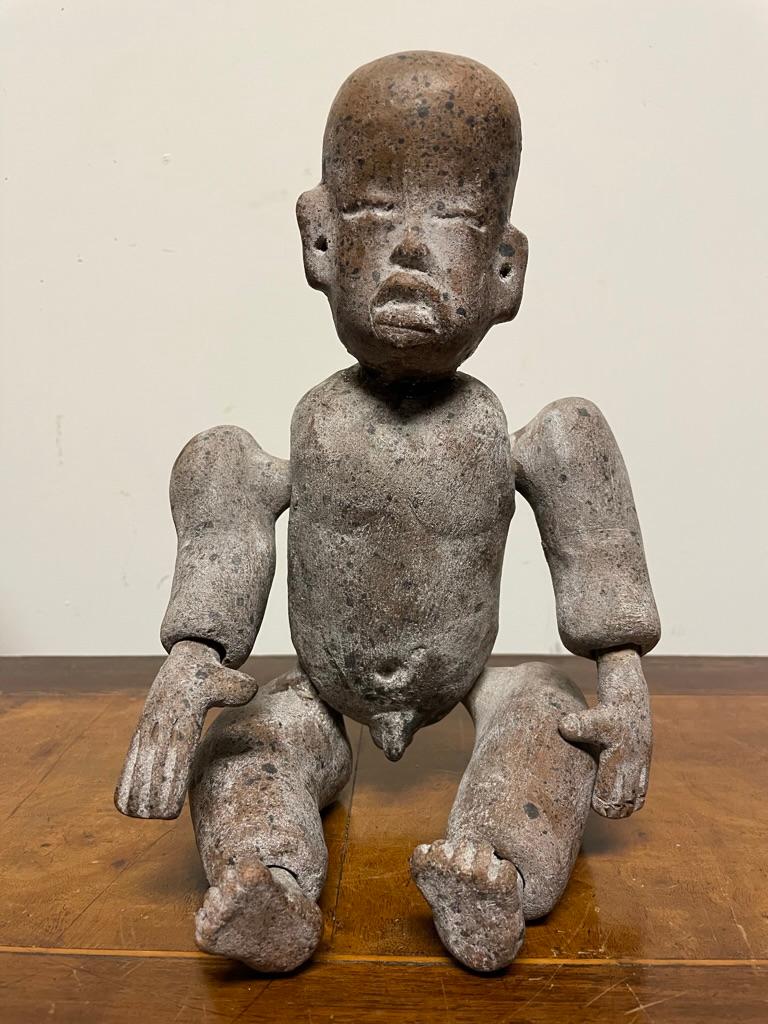 A Pre-Columbian Olmec style pottery figure of a boy with articulated arms and legs. The youthful body carefully modeled with soft belly and broad shoulders, the head with prototypical Olmec full cheeks, narrow eyes and fleshy down turned mouth.