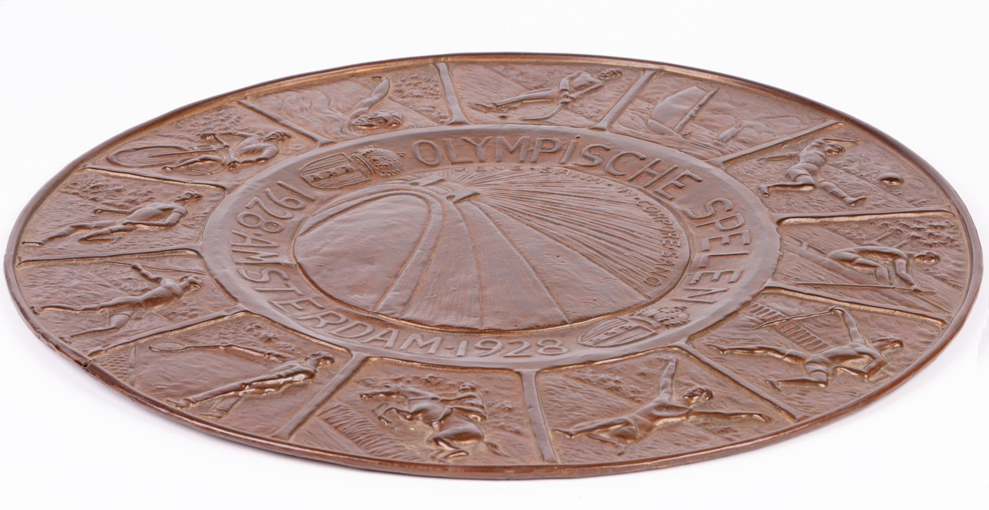 A scarce and wonderful Art Deco bronzed pressed metal wall plaque commemorating the Olympic Games held in Amsterdam in 1928. The plaque is of large round shape and made of a light pressed metal with a simple round folded rim, the surface with a