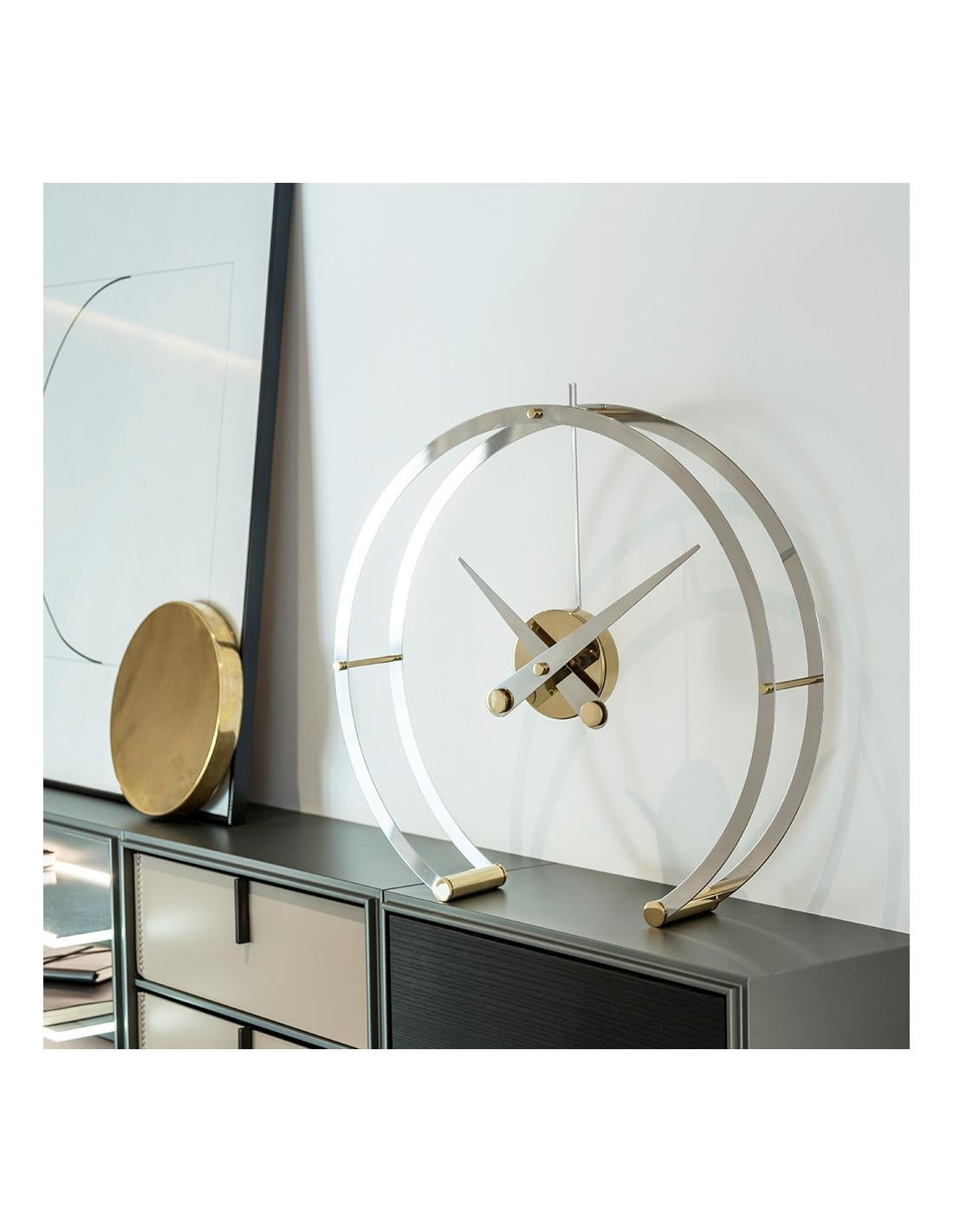 The Omega G Clock impresses by keeping a clock suspended in the air while losing its depth by removing unnecessary items and making it simple and glamorous .
Omega G table clock : Rings and hands in stainless steel with gold details, box in