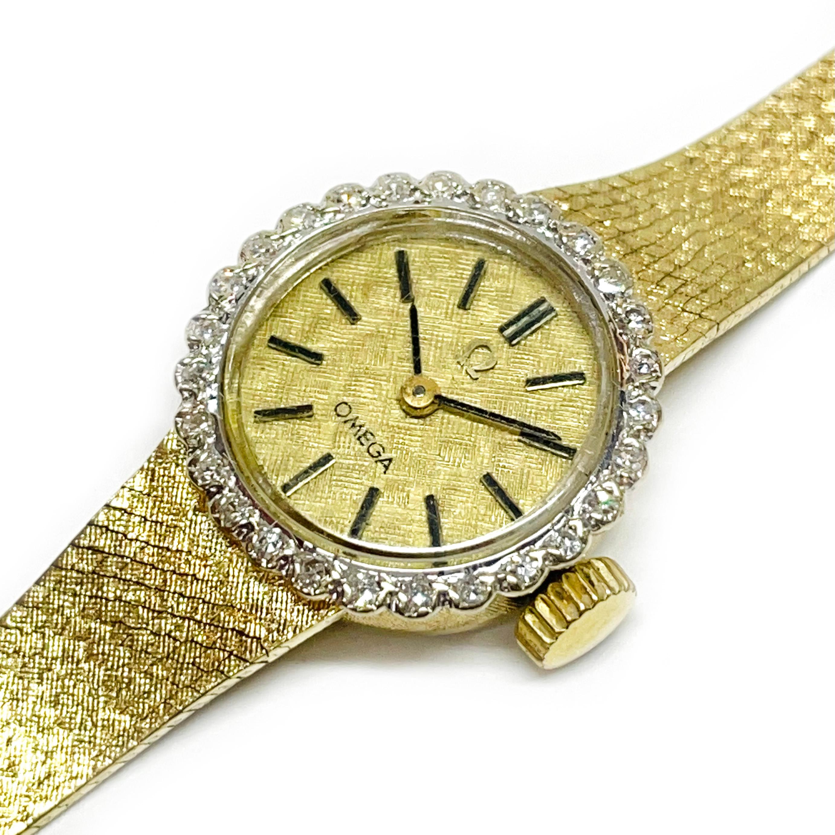 Omega Ladies 14 Karat Yellow Gold Diamond Wristwatch. The watch features a round gold dial with hour and minute hands, and twenty-seven round diamonds surrounding the dial. The diamonds have a total carat weight of 0.025ctw. The 14k yellow gold