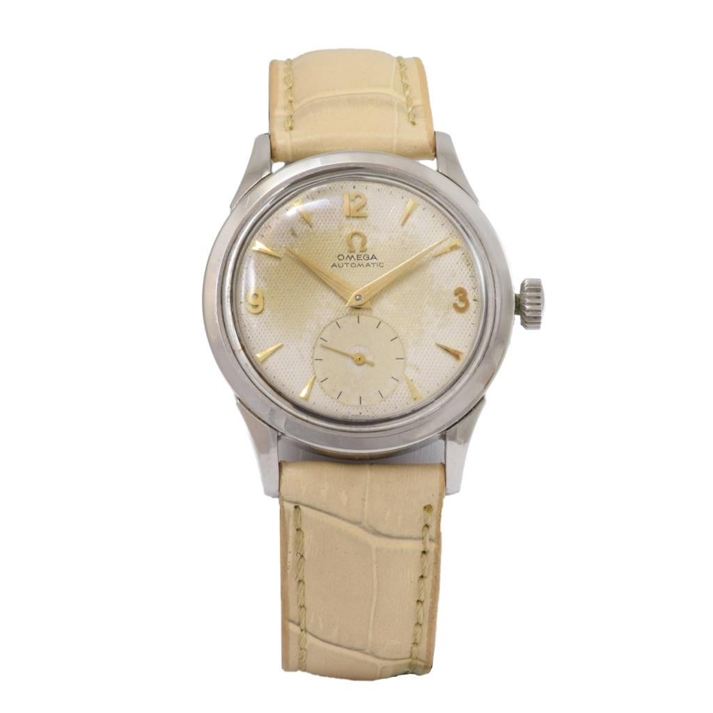 Découvrez l'élégance intemporelle de la montre automatique OMEGA Vintage 1950's en acier inoxydable. Son boîtier rond de 34 mm, son cadran beige en nid d'abeille avec index en or et sa trotteuse à cadran auxiliaire témoignent d'une sophistication