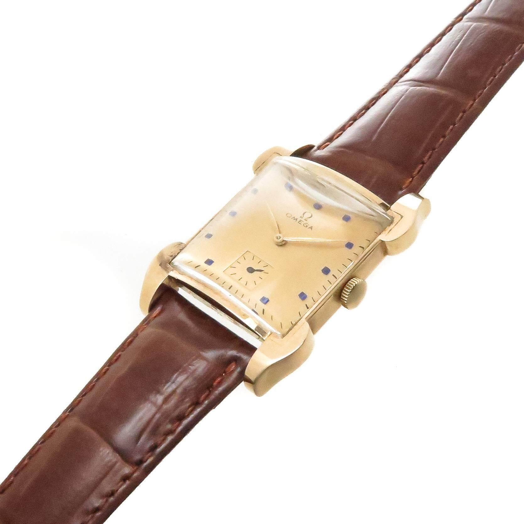 Circa 1940s Omega Wrist Watch, 18K yellow Gold 2 piece case with eccentric curved Lugs measuring 38 MM from Lug end to end and 30 MM wide. 17 jewel Mechanical, Manual wind movement, Gold dial with applied Synthetic Blue Sapphire markers and a sub