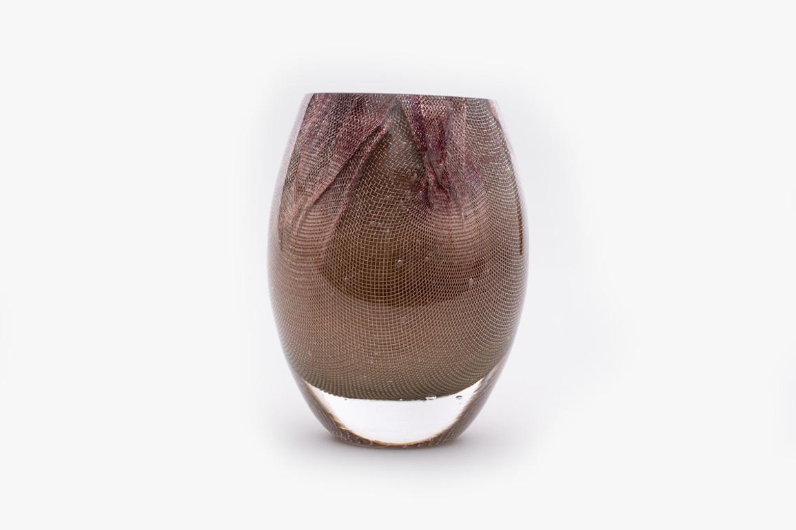 84.2 Copper Mesh Glass Vase is created by suspending a bubble of coloured glass within a fine copper mesh basket that is then plunged into hot clear glass. Air is blown into the matrix to gently push the white glass through the mesh, creating a