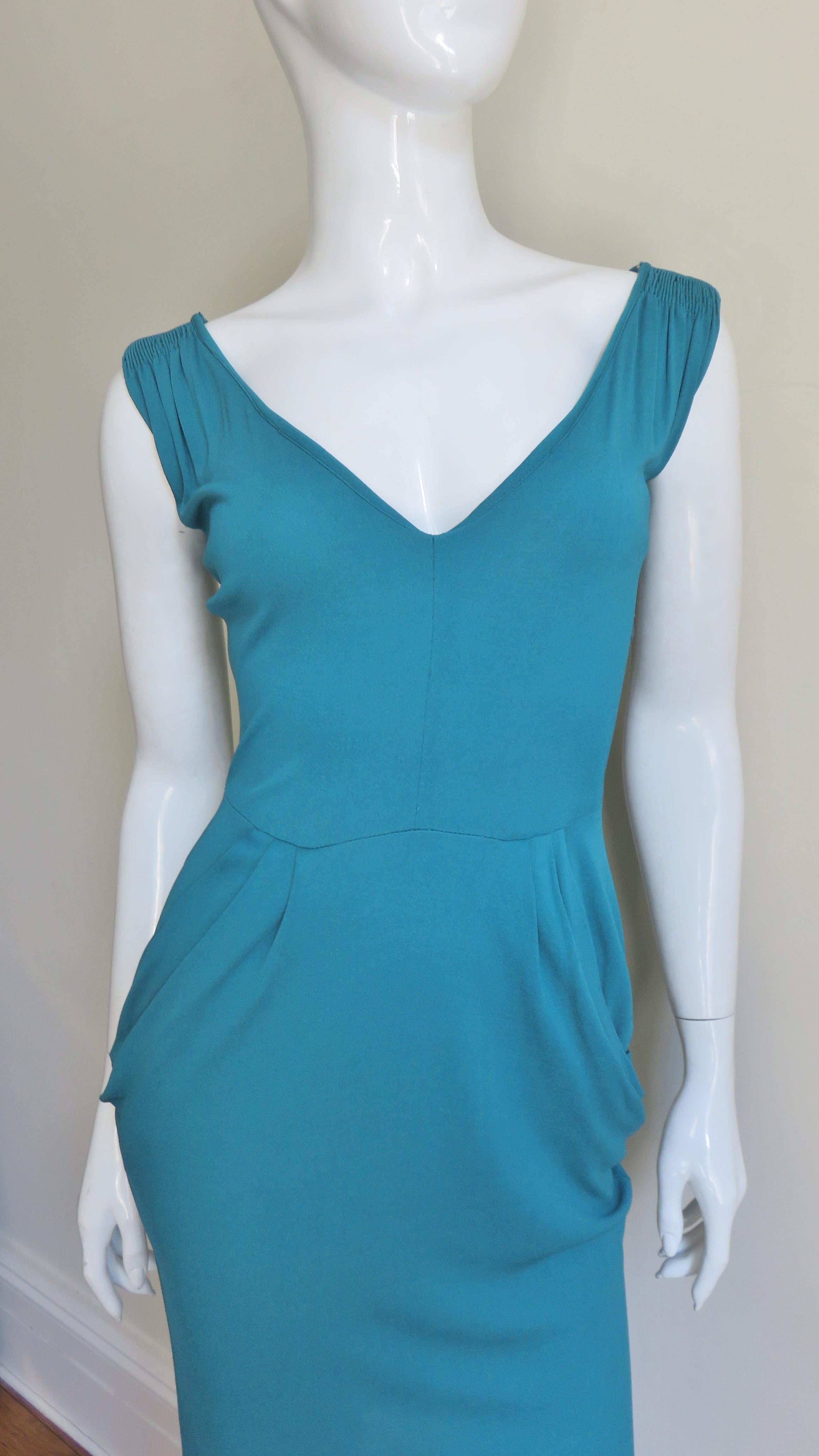 A beautiful turquoise jersey dress from Norma Kamali's Omo collection. It is sleeveless with a V neckline, hip pockets and the skirt narrows towards the hem.  It has a matching side zipper and is unlined.  
Fits sizes Extra Small, Small.

Bust 