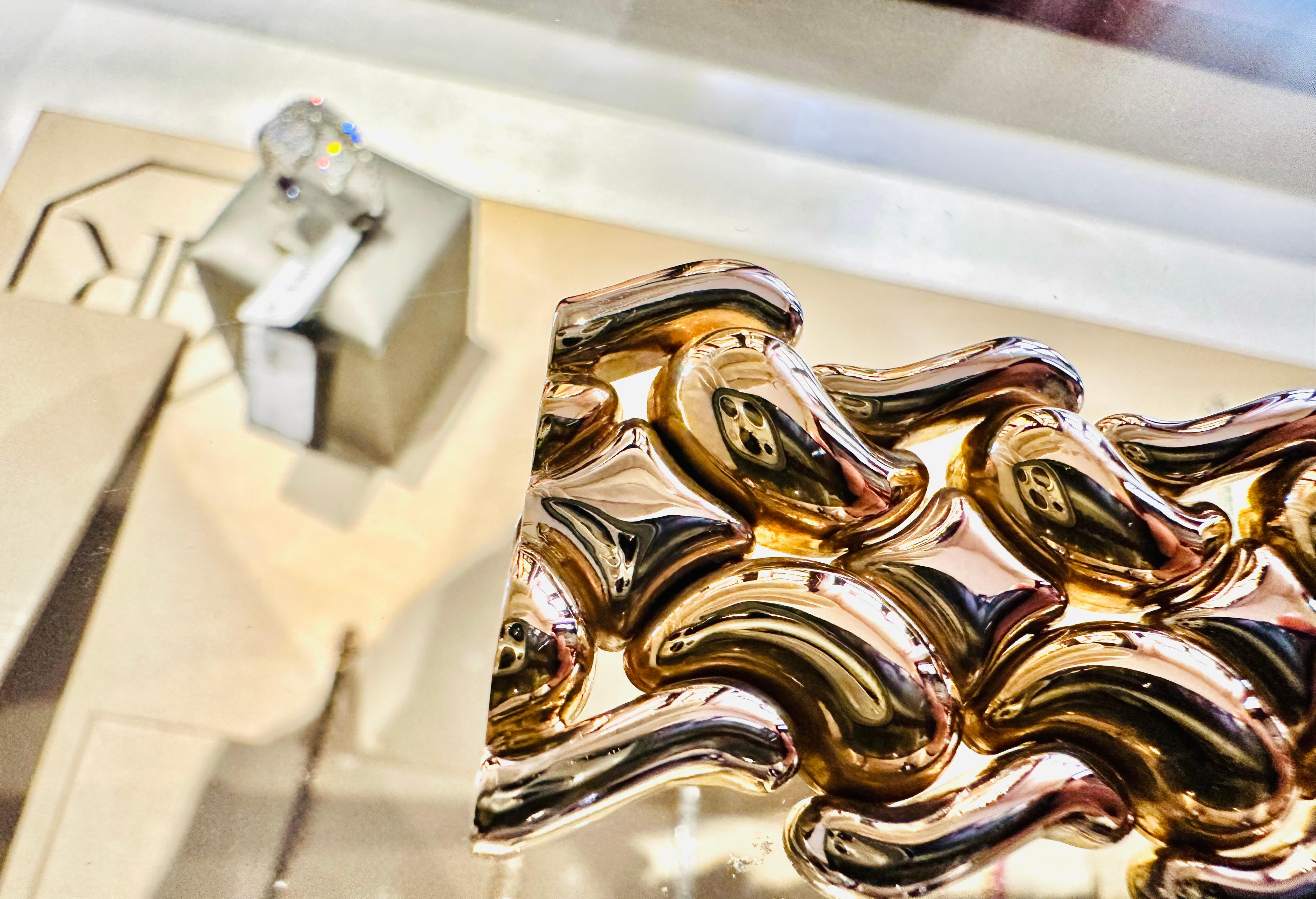 Questo straordinario bracciale in oro bianco e giallo 18 carati è una vera scultura di luce e movimento. Le sue linee sinuose e voluttuose sembrano catturare il fluire delle onde, trasformando il metallo prezioso in un capolavoro vivo e vibrante.
