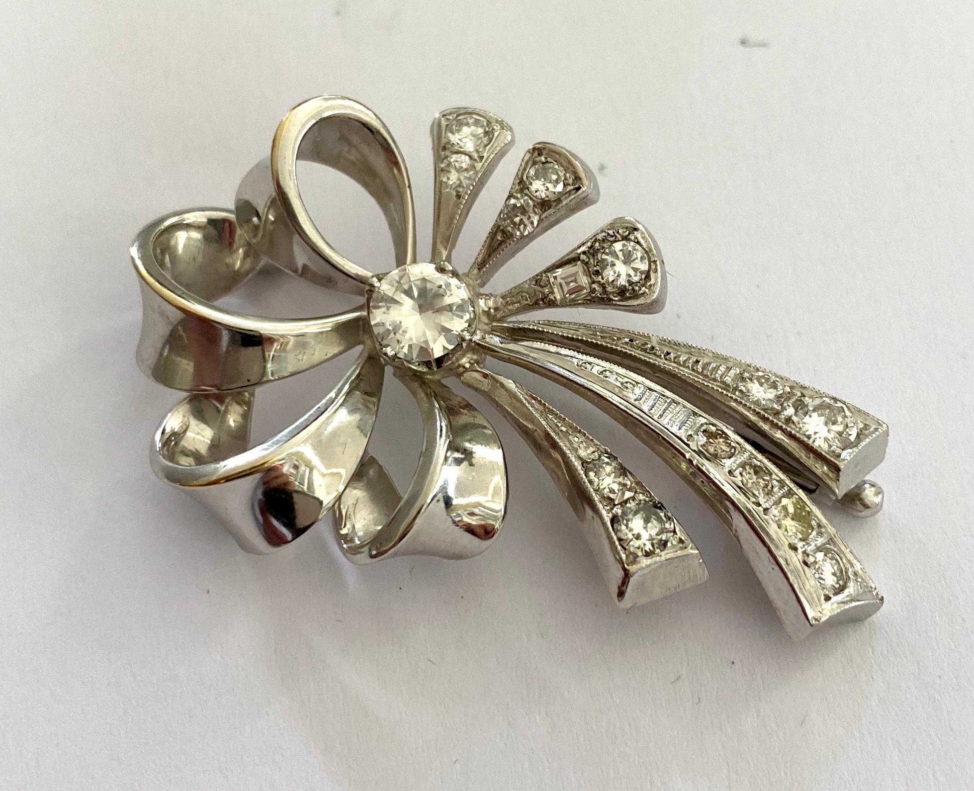 One (1) 14K. white Gold Bow Brooch, made in Holland ca. 1950
set with:
One (1) Round Brilliant Cut Diamond: 0.56 ct SI2 - G
Fourteen (14) roud Brilliant and Baquette cut diamonds: 0.93 ct VS P1 - G-M 
Mesurements of the Brooch: 46 x 28 x 6 mm
Weight