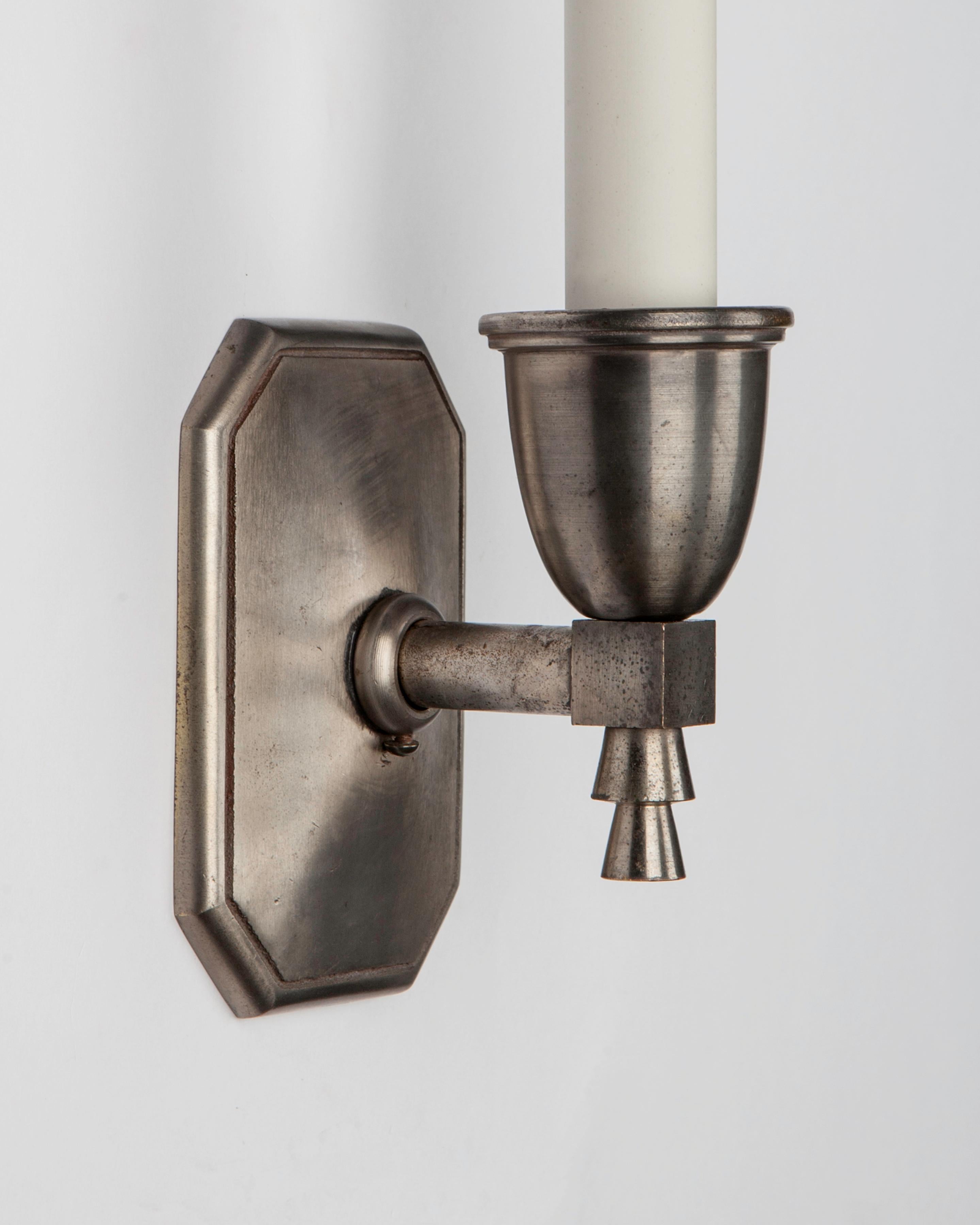 AIS3113
A pair of vintage single-light Art Deco period sconces in their original aged nickel finish over bronze. The rectangular backplates with chamfered edges and the round candle cup terminating in a stepped tapered cylindrical finial. Signed by