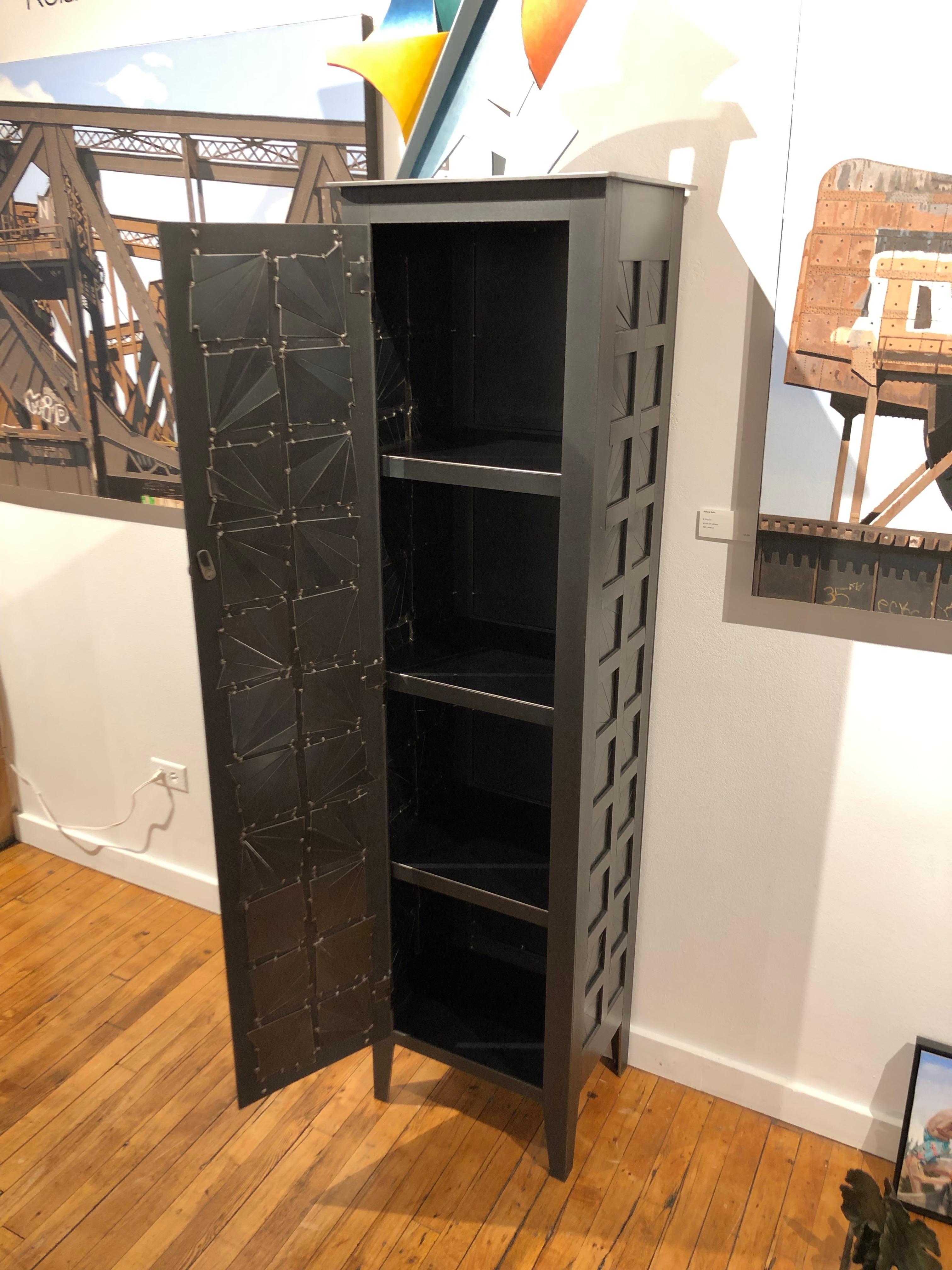 This is a totally functional tall one door cupboard. It created from hot-rolled steel panels. The panels on the door front and sides are made from welded pieces of steel arranged in a fractured starburst quilt pattern. The pattern is inspired by the
