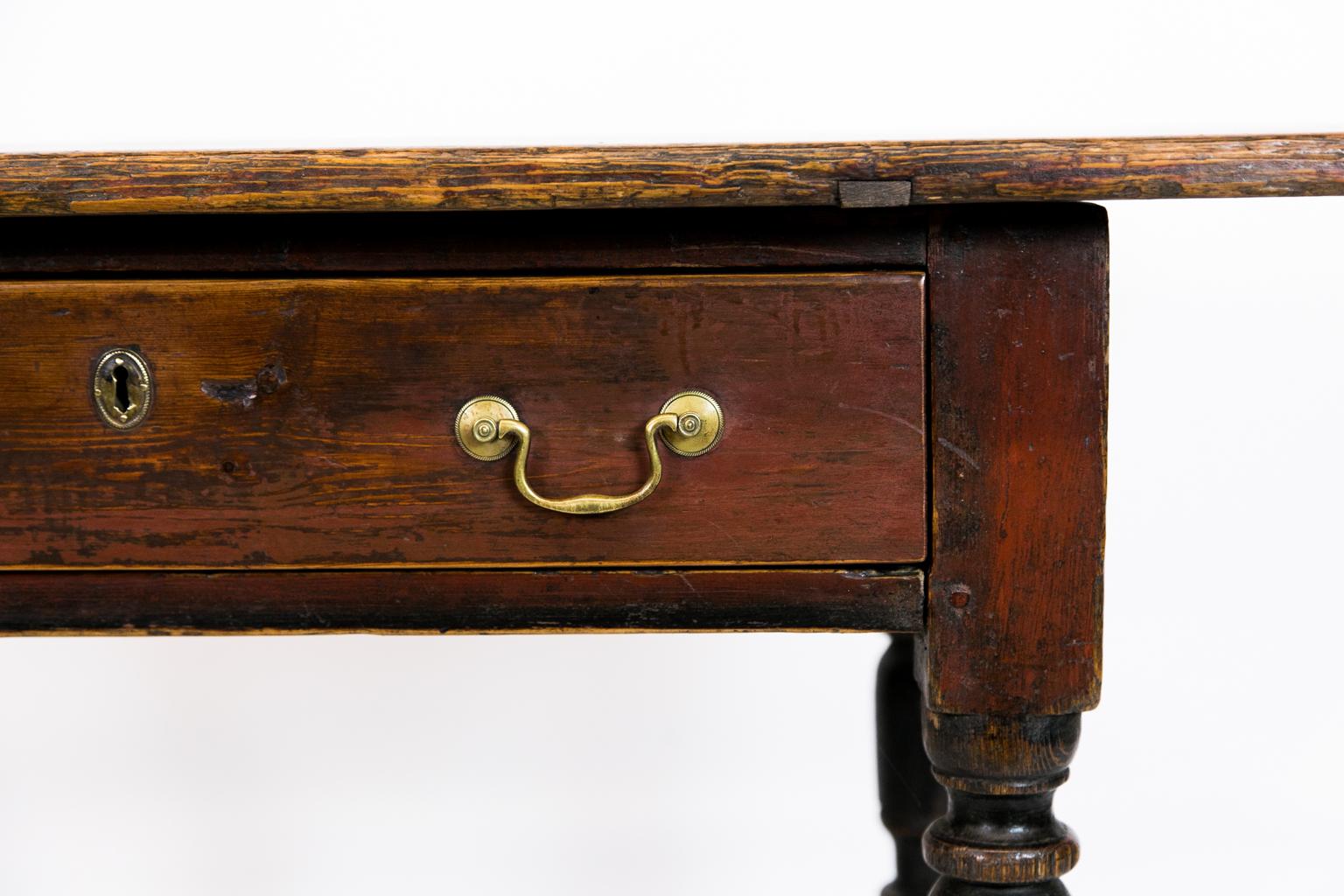 One-drawer pine tavern table has traces of the original red paint on the top, drawer, and part of the top of the legs. The lower part of the legs and stretchers have traces of black paint, and there is exposed peg construction.
    