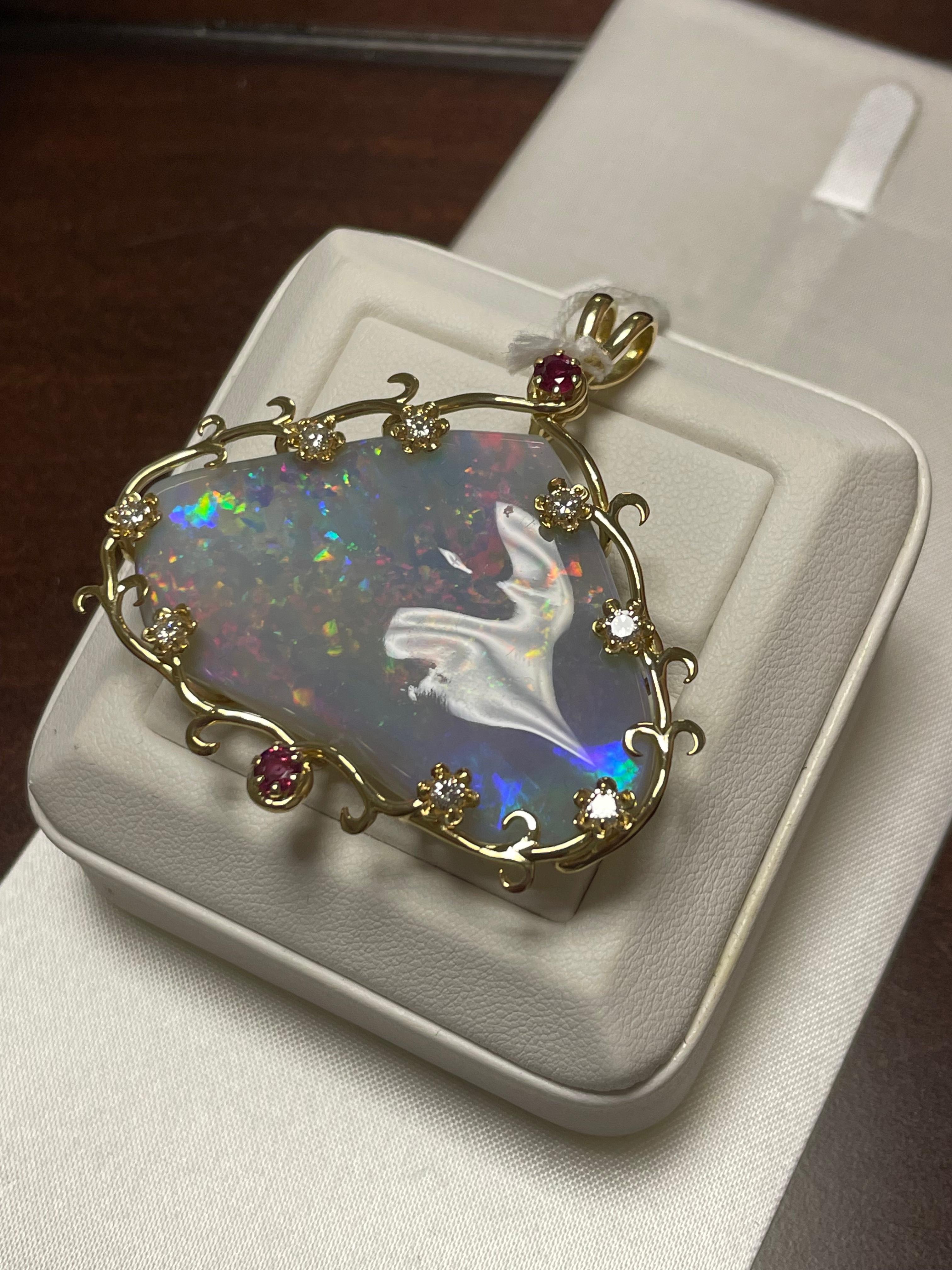 One lady's opal, diamonds, and rubies pendant.  Opal is semi-crystal and multicolor with dull saturation scale.  Includes pinfire pattern and din brightness of fire. Cut into cabochon shape and freeform.  Measurements of opal are 48.0 x 26.0. Eight