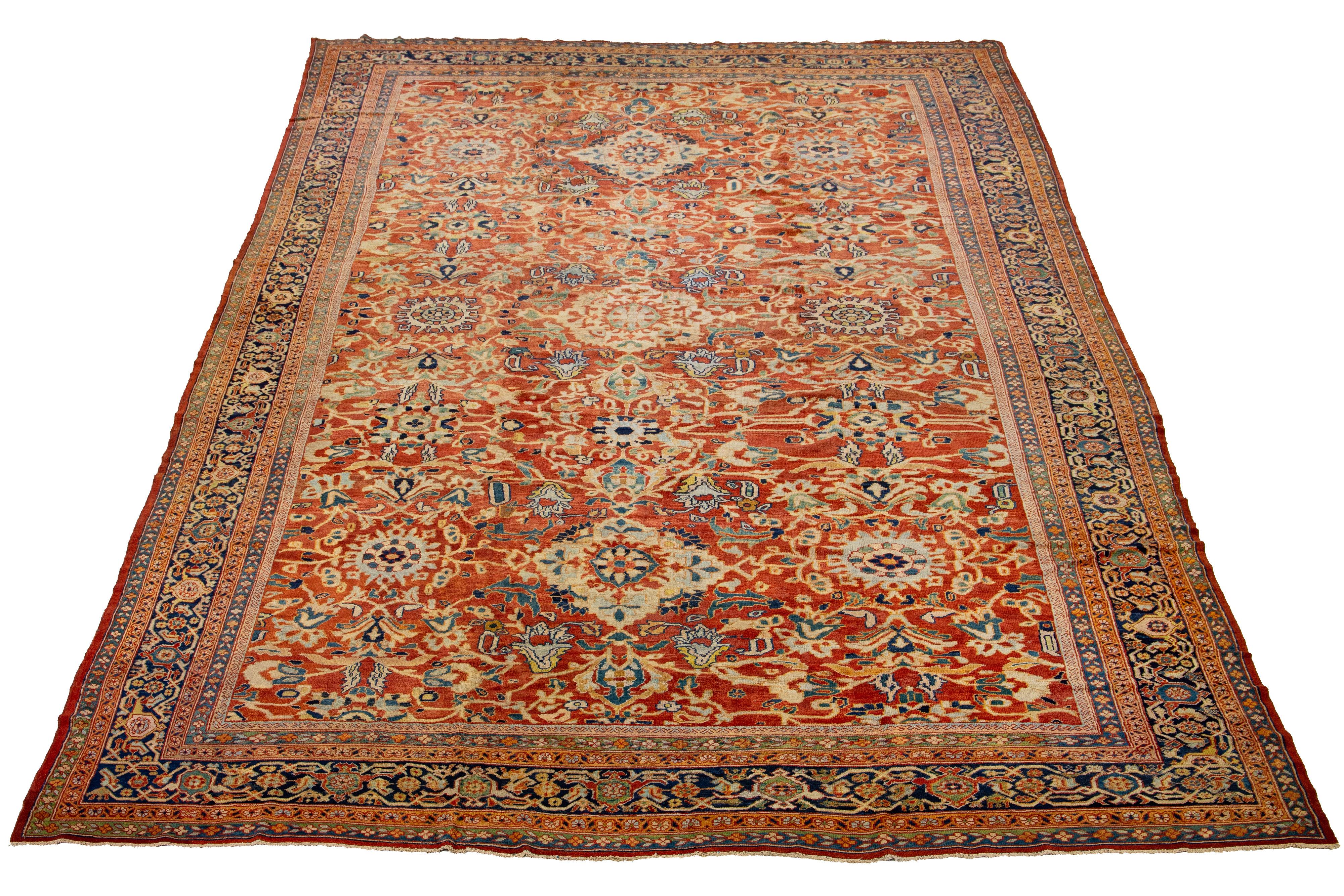This stunning one-of-a-kind hand-knotted wool rug is an antique oversized Sultanabad from the 1890s. It features a red rust field with multicolored accents in a floral design. The strong wool weave of this classic rug design is achieved through