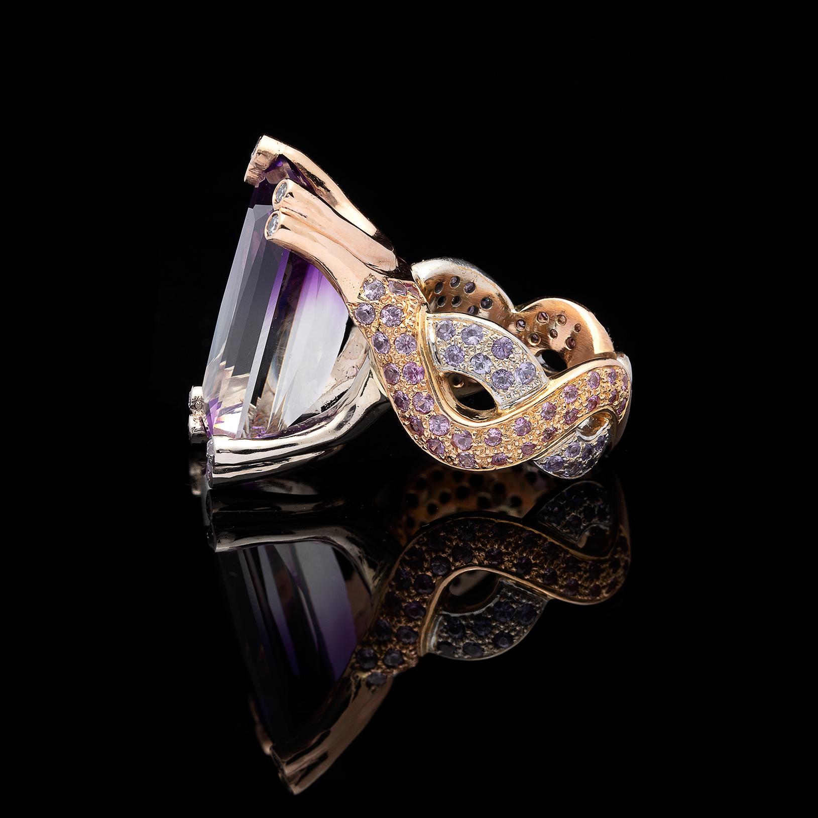 Custom designed and handmade, this ring features a unique bi-color rectangular-cut 20-cts. amethyst, displaying purple and white flashes of color. The 18k rose and white gold snaked mounting is pave-set with 88 round pink and purple sapphires, and