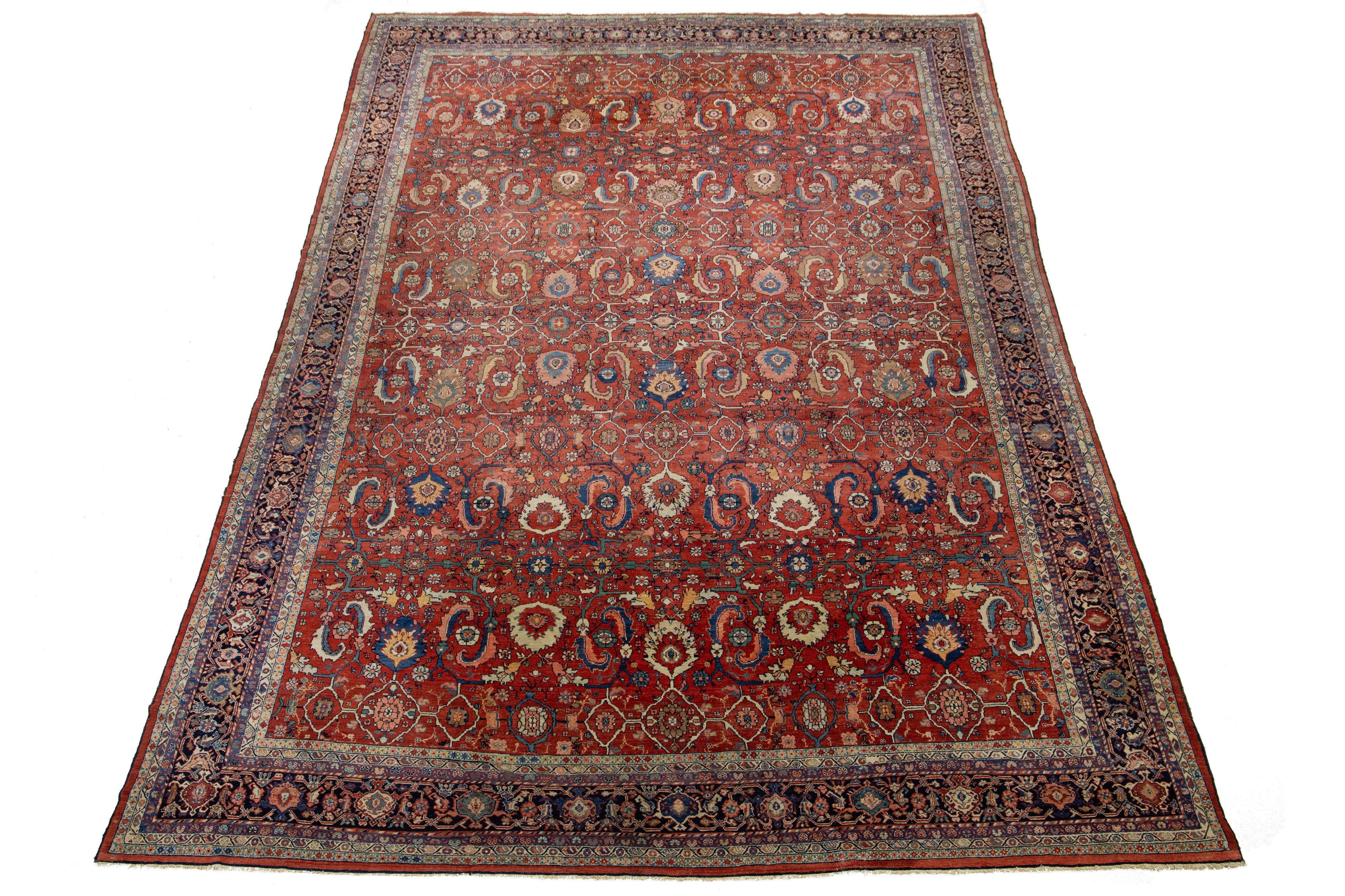 Ce tapis unique en laine nouée à la main est une antiquité surdimensionnée de Sultanabad, datant des années 1870. Il présente un champ rouge richement décoré d'accents floraux multicolores. Le robuste tissage de laine de ce tapis classique est le