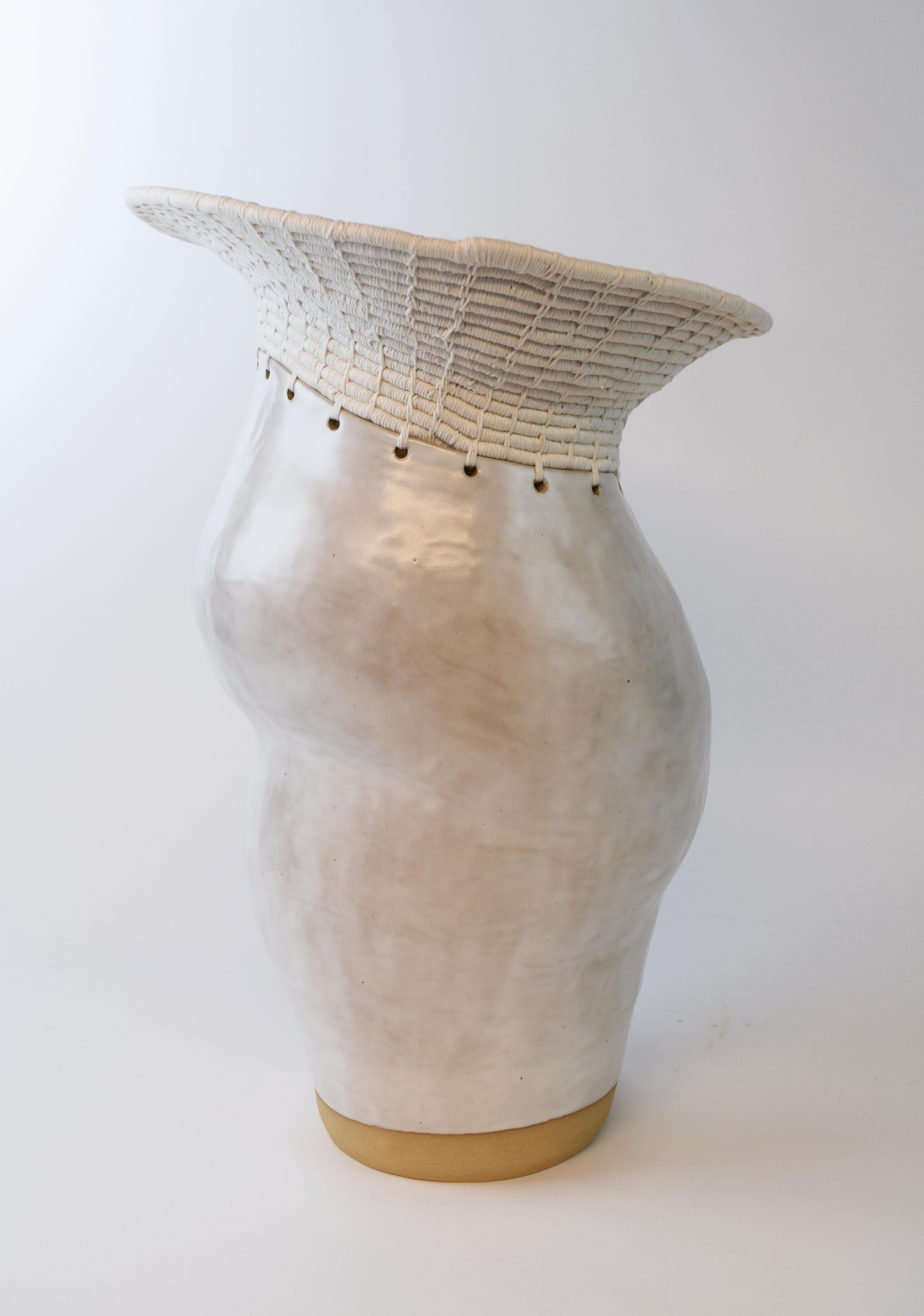 Handgeformtes, asymmetrisches Gefäß aus Steinzeug mit satinweißer Glasur. Der obere Teil des Gefäßes ist aus weißer Baumwolle gewebt, was das Zusammenspiel von Keramik und Fasern verdeutlicht. 

Maße: 18,5 