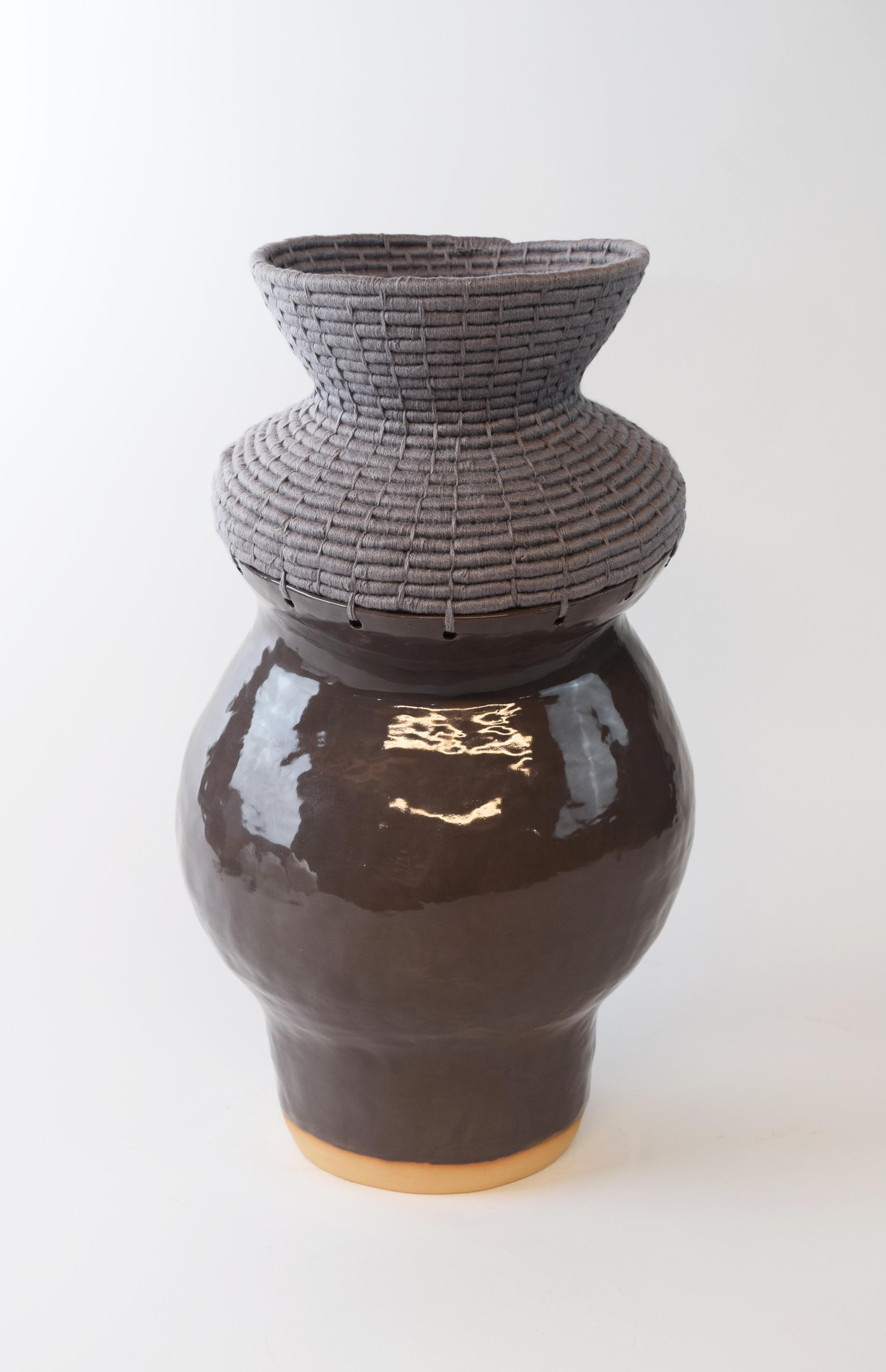 Hand formed asymmetrical stoneware vessel with gloss charcoal glaze. The top part of the vessel is woven in gray cotton, showcasing the interplay of ceramic and fiber. 

18”H x 9”W

One of a kind collections with a limited number of pieces are