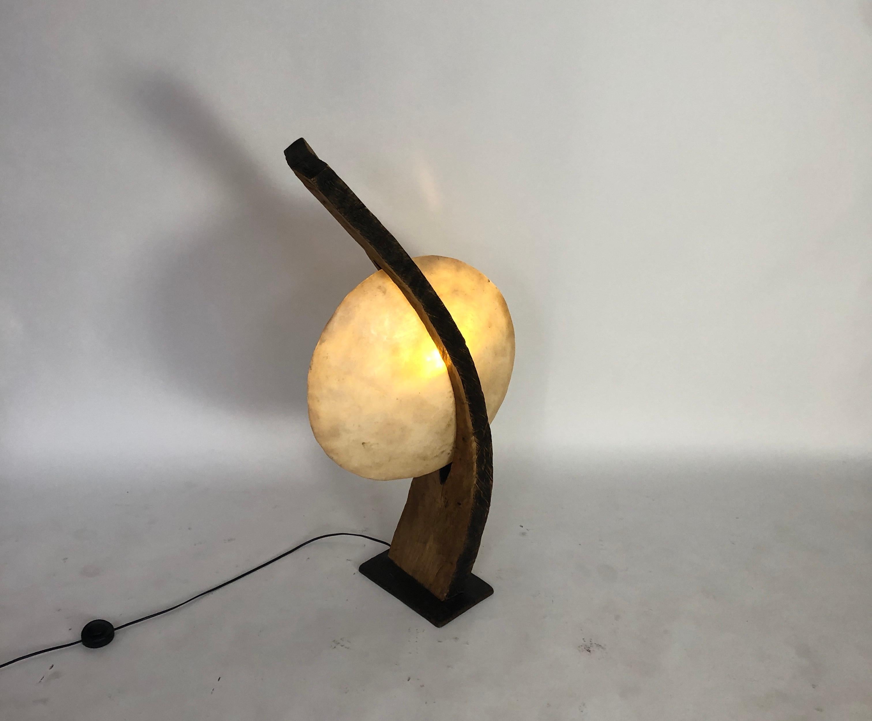 This one of a kind creation by Jerome Pocheron is crafted by a massive bent slap of wood, which is fitting with a convex disc. The disc is made of a resin composition which conceals the light bulb within. The soft light which is given off make is a