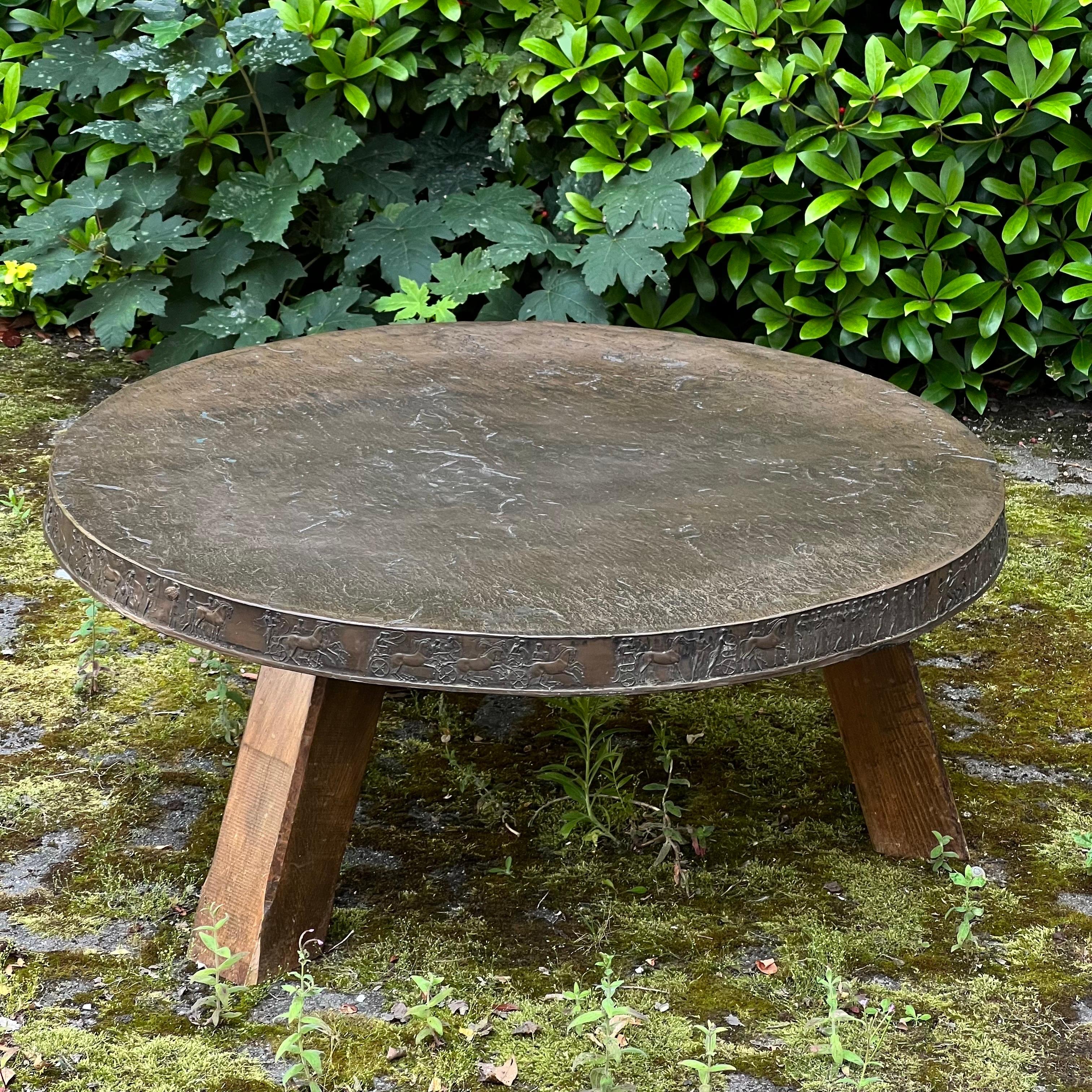 One of a kind round three legged bronze and oak coffee table. Showing elegant antique scenes details on the sides with a detailed textured top. Even the under top is made partially of bronze. Three oak brown stained legs fixed with 4 screws. Not a