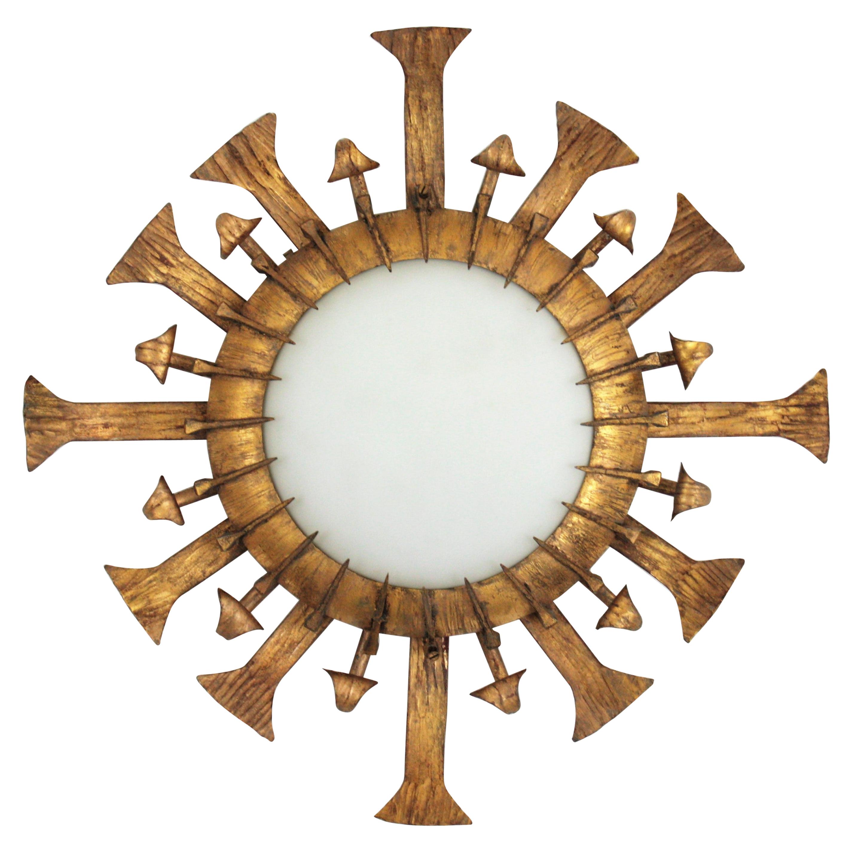 Rare Brutalist sunburst light fixture in gilt wrought iron with milk glass shade. France, 1940s-1950s
This hand forged iron sunburst flush mount or wall sconce has an eye-catching design with alternating rays and scrolled details. The central milk