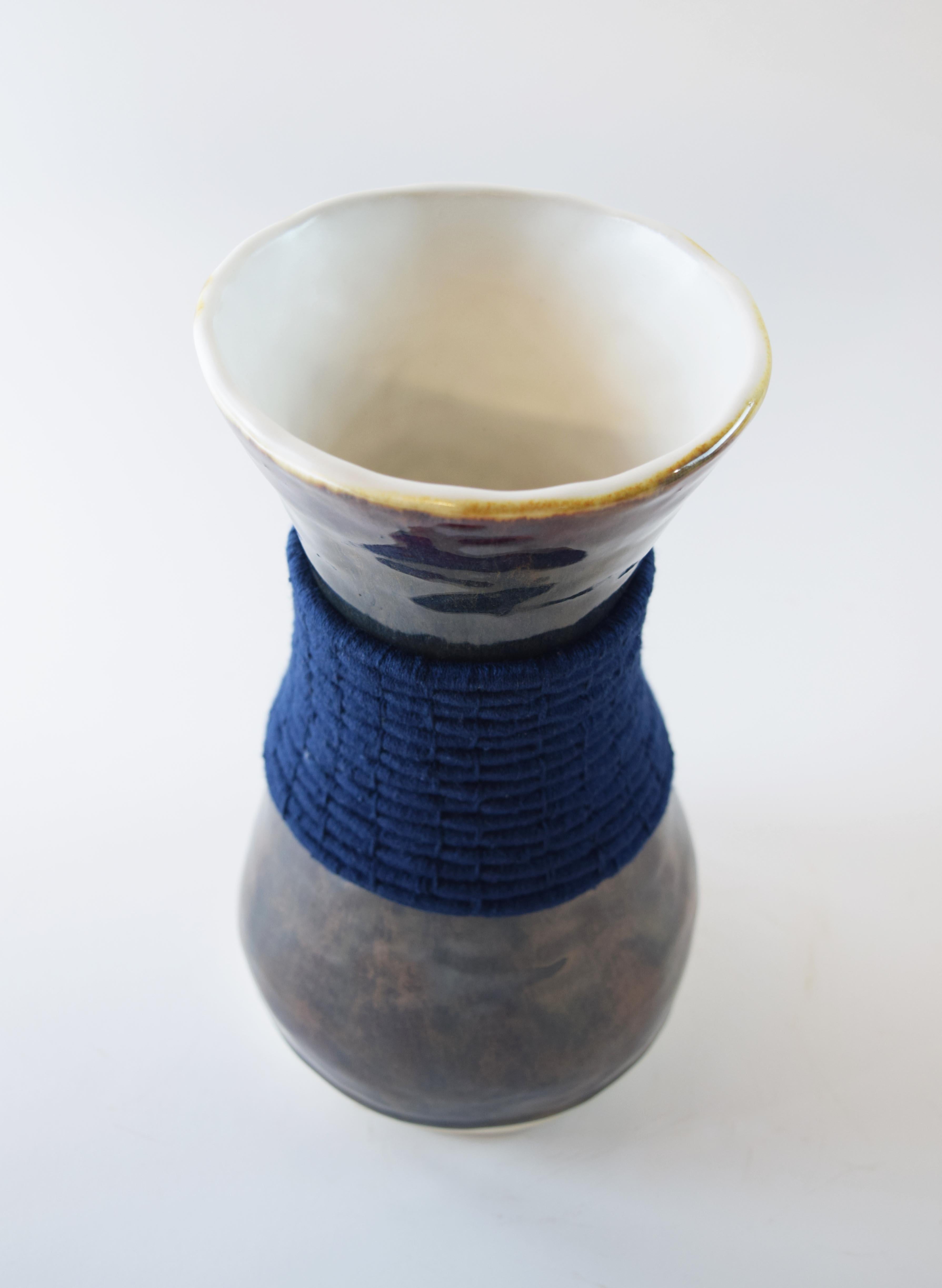 Vase #768 by Karen Gayle Tinney

Hand formed stoneware vase with a multi-colored glaze that appears in tones ranging from red to brown to blue. Woven navy cotton detailing around outside of vessel. Vase is water tight.

10”H x 5.5”W

One of a