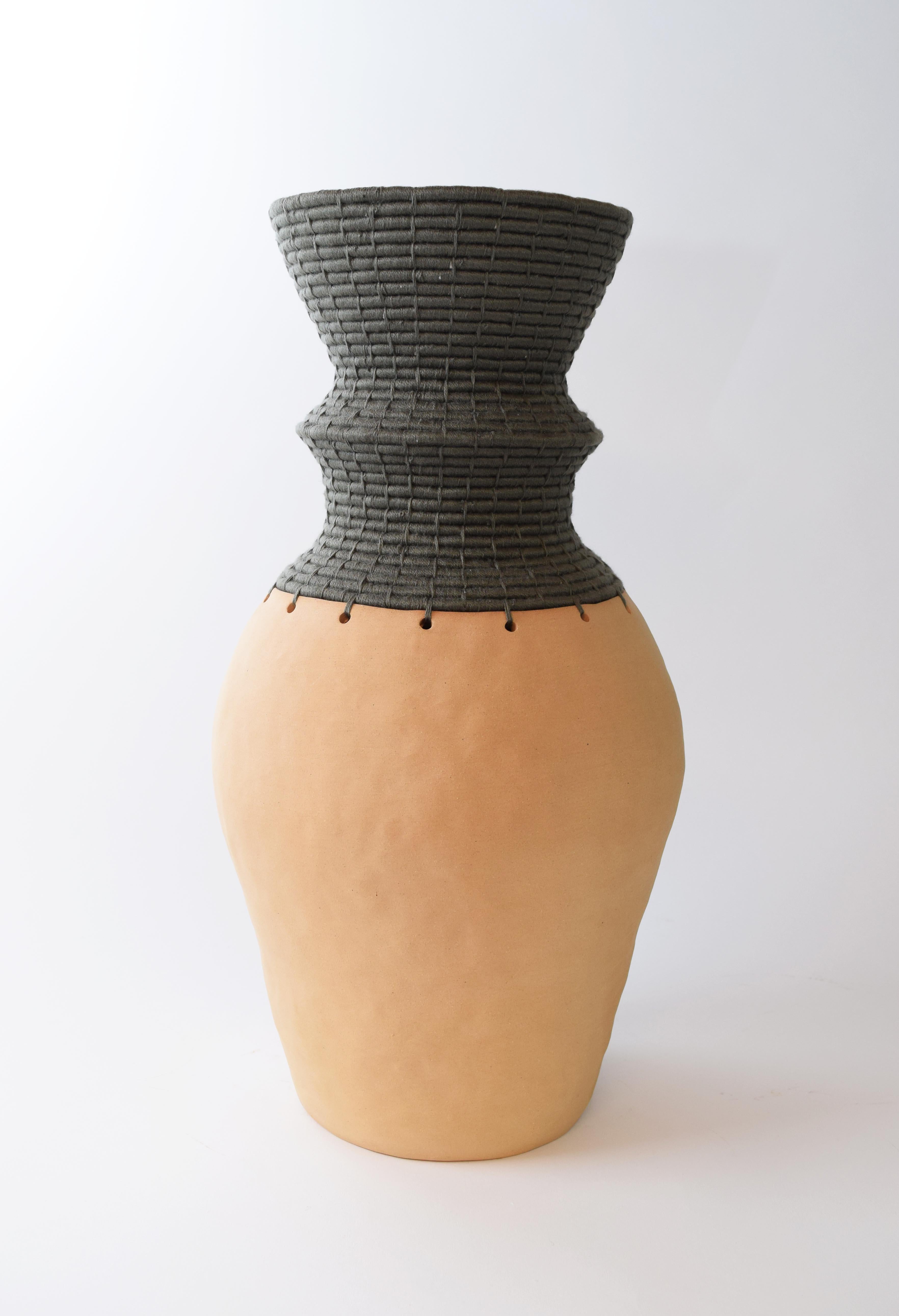 Hand formed stoneware vessel which was left unglazed, exposing the natural color of the clay. The top part of the vessel is woven in olive cotton.

Measures: 17.5” H x 9” W

One of a kind collections with a limited number of pieces are released