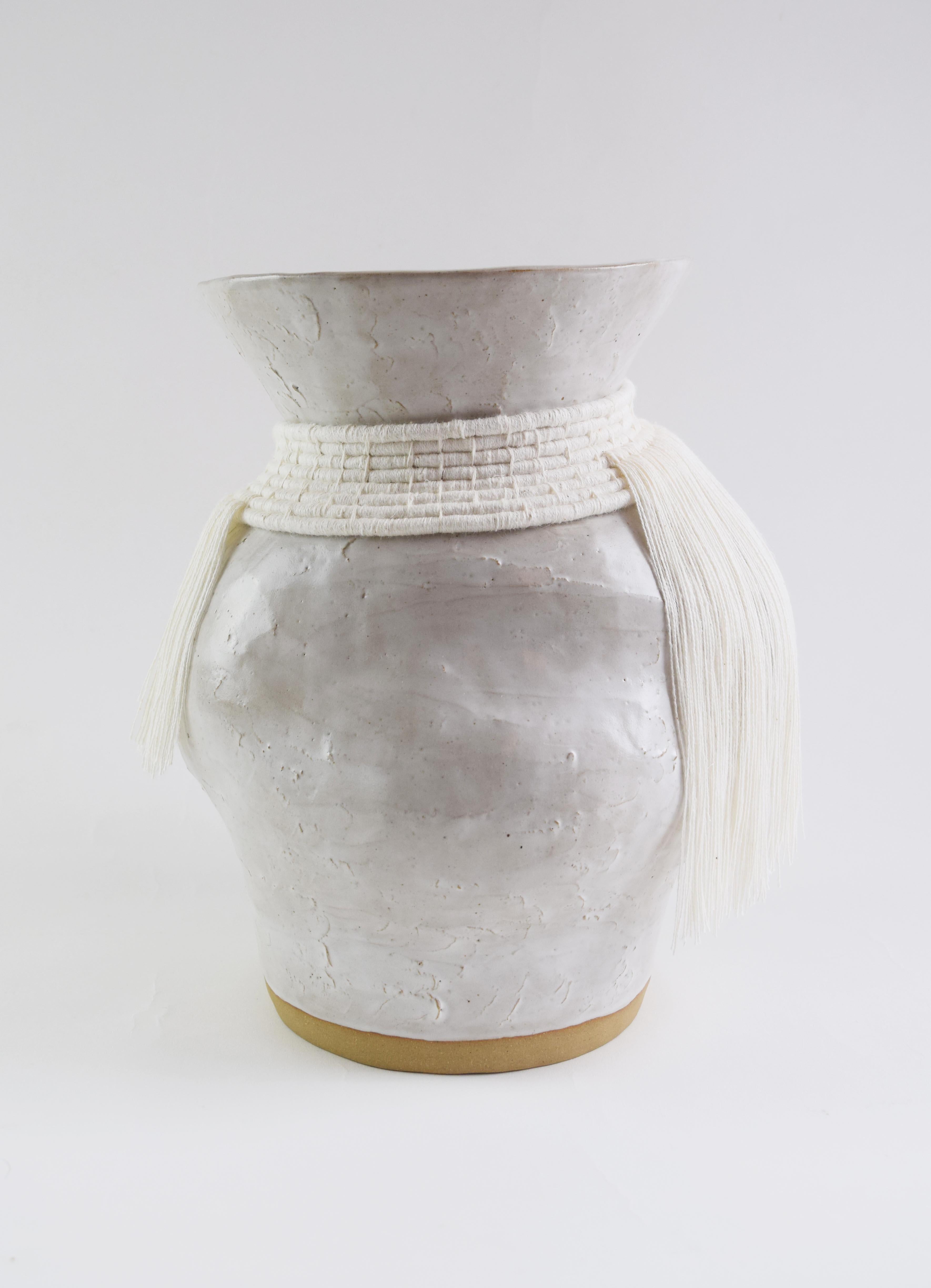 Vaso in gres formato a mano con smalto bianco.  Dettagli in cotone bianco intrecciato all'esterno con frange. Il vaso è a tenuta stagna.

12 