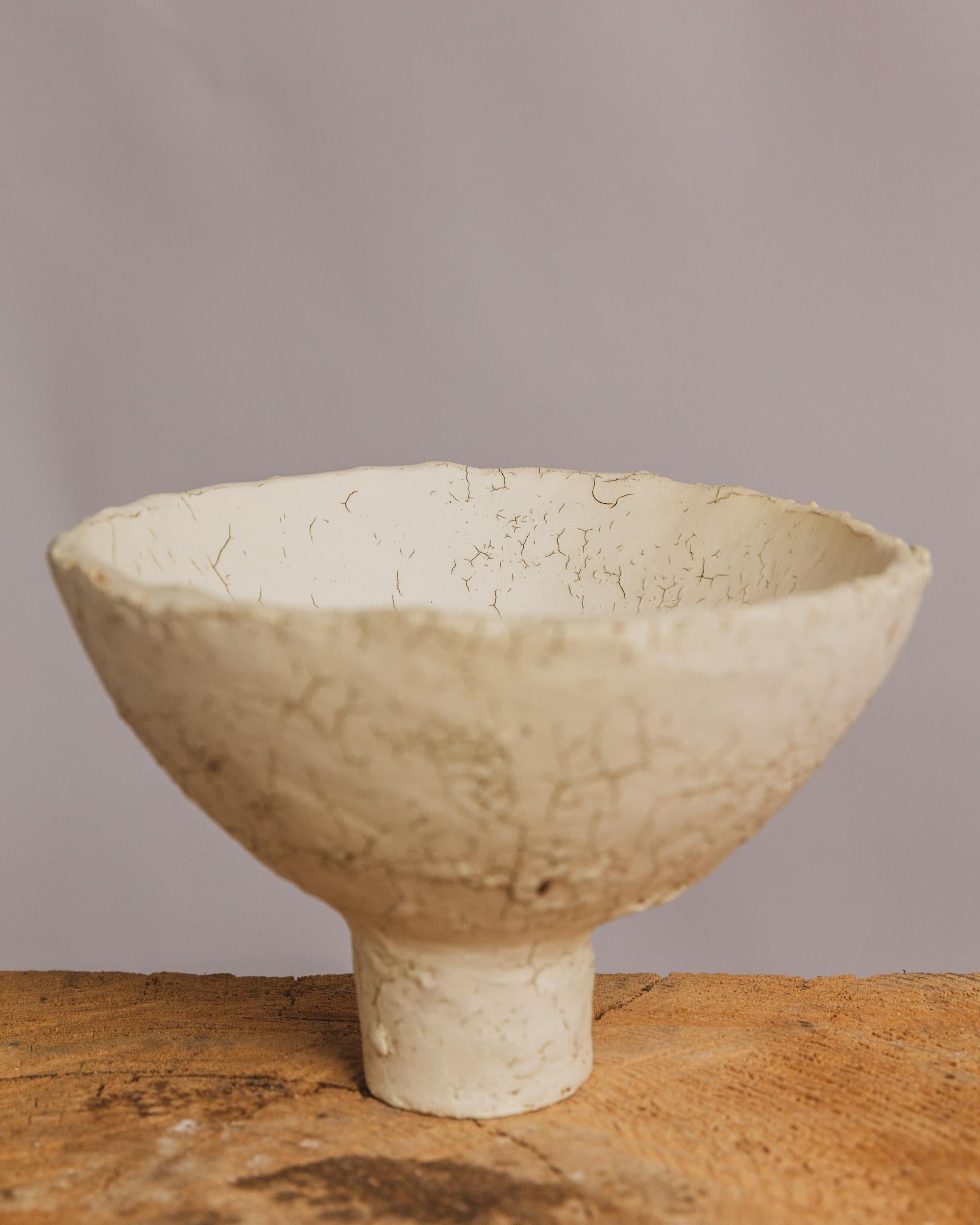 This handbuilt ceramic compote vessel by Ilona Golovina is a poetic meditation on surface tension, time, and subtle transformation. Raised on a cylindrical foot, the bowl’s minimalist form contrasts with its richly textured surface—a natural crackle