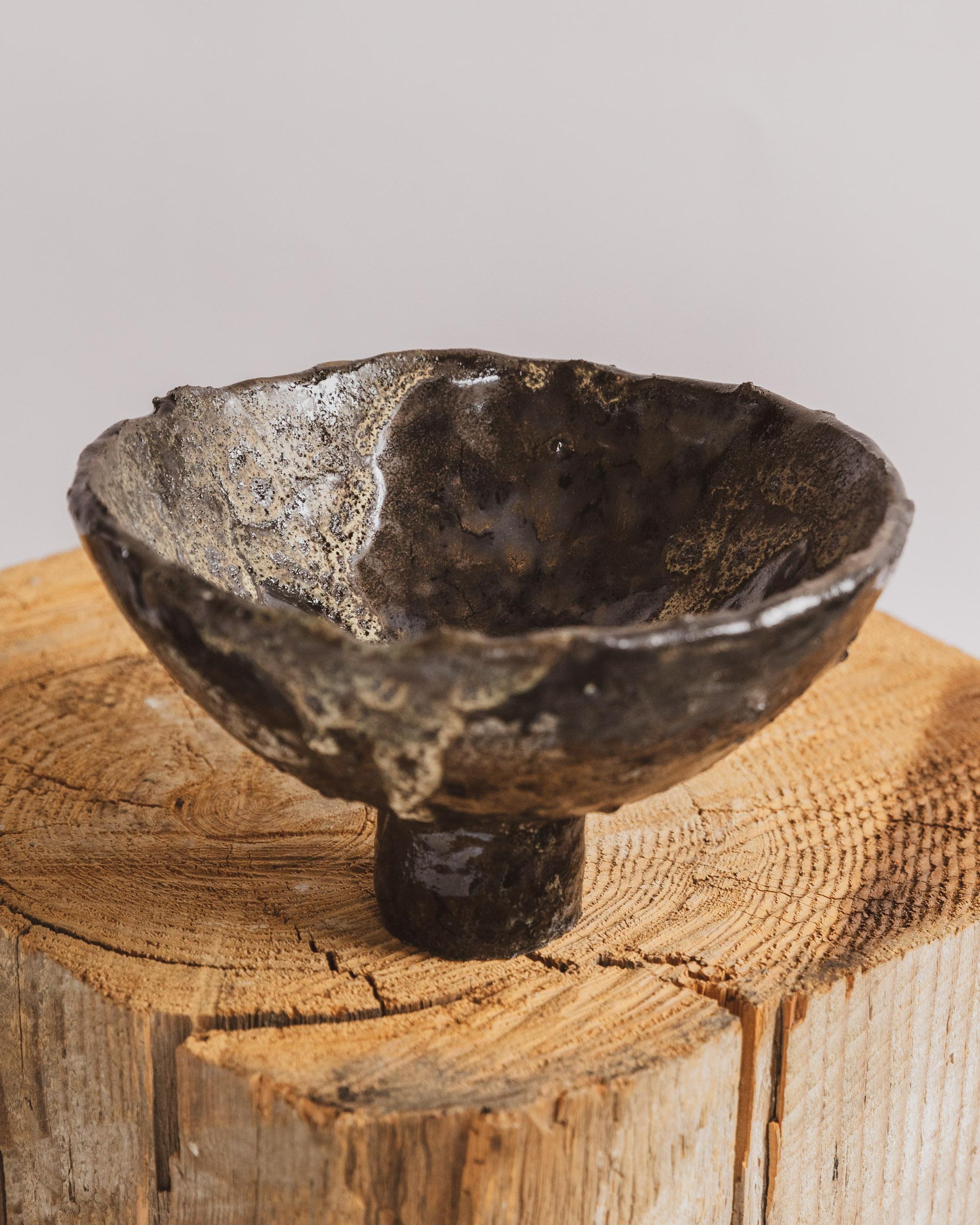 This handbuilt footed compote vessel by Ilona Golovina is a striking fusion of elemental texture and sculptural refinement. Elevated on a cylindrical base, the bowl’s organic form and uneven rim speak to the artist’s embrace of imperfection and
