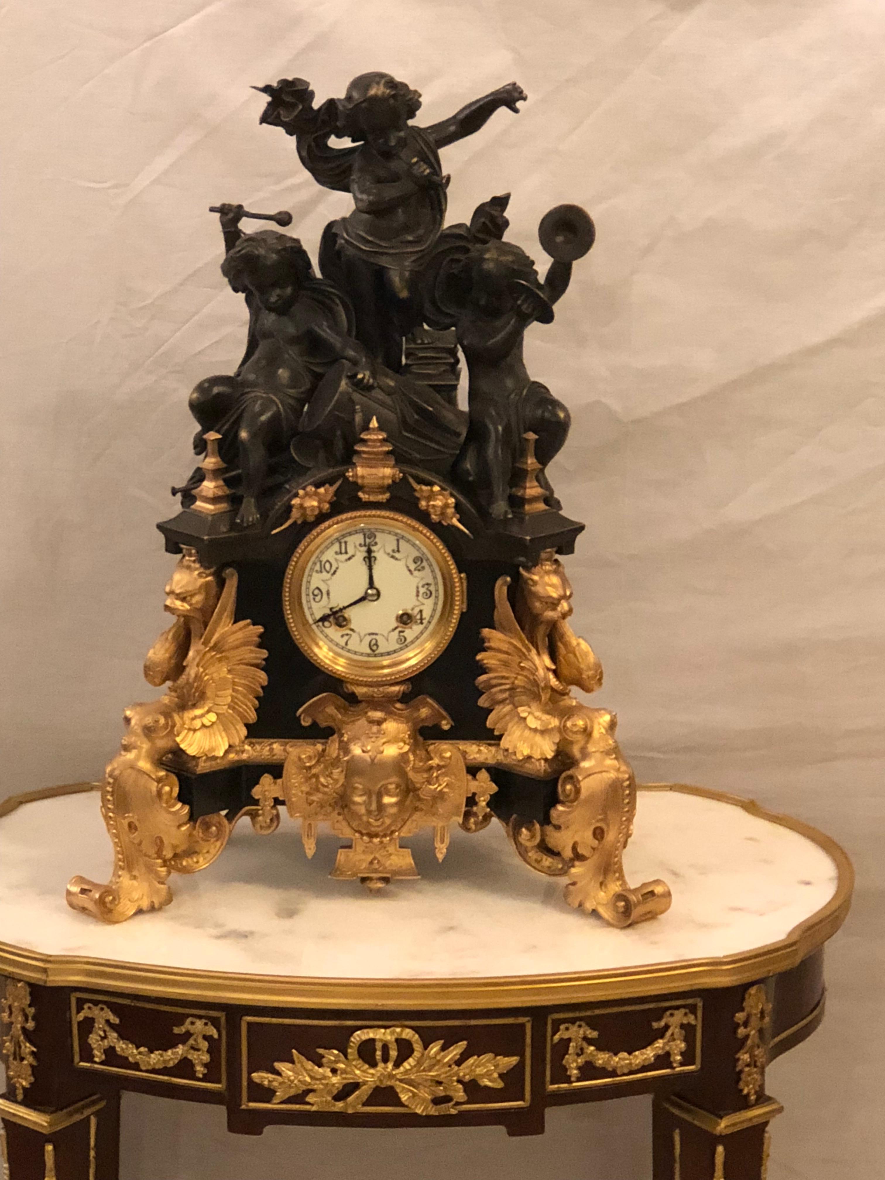 One of a kind French patinated and doré bronze figural mantle clock. In working condition with key this palatial mantle clock has a special musical theme showing three cherubs playing instruments atop a pedestal base of griffins. 

hXAX / Exxx.