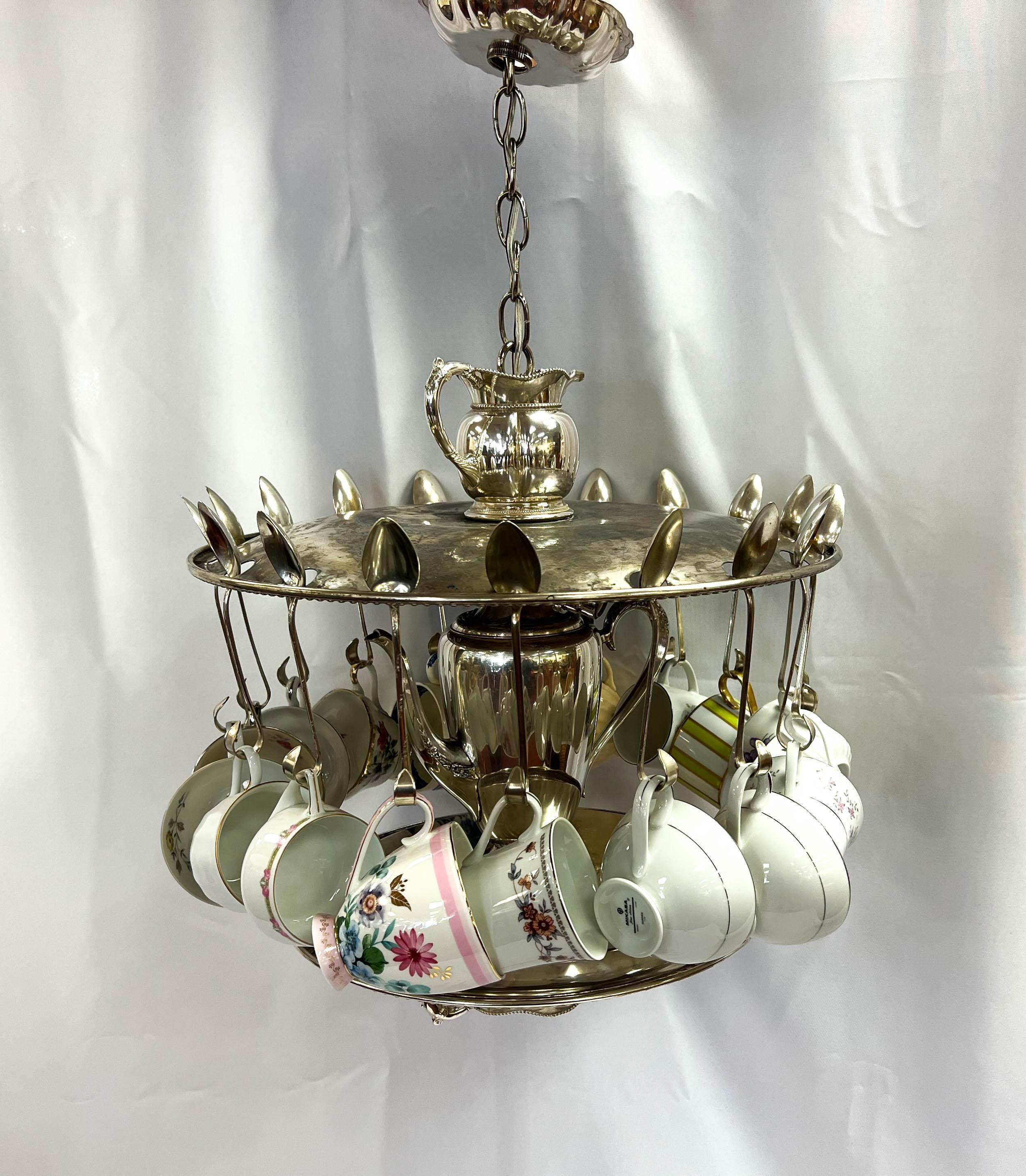 Hand-crafted novelty chandelier made entirely from silver plate service pieces, adorned with an assortment of porcelain teacups. Cups may be switched out to match your decor or rearranged as they hang freely on this fixture. A perfect light fixture