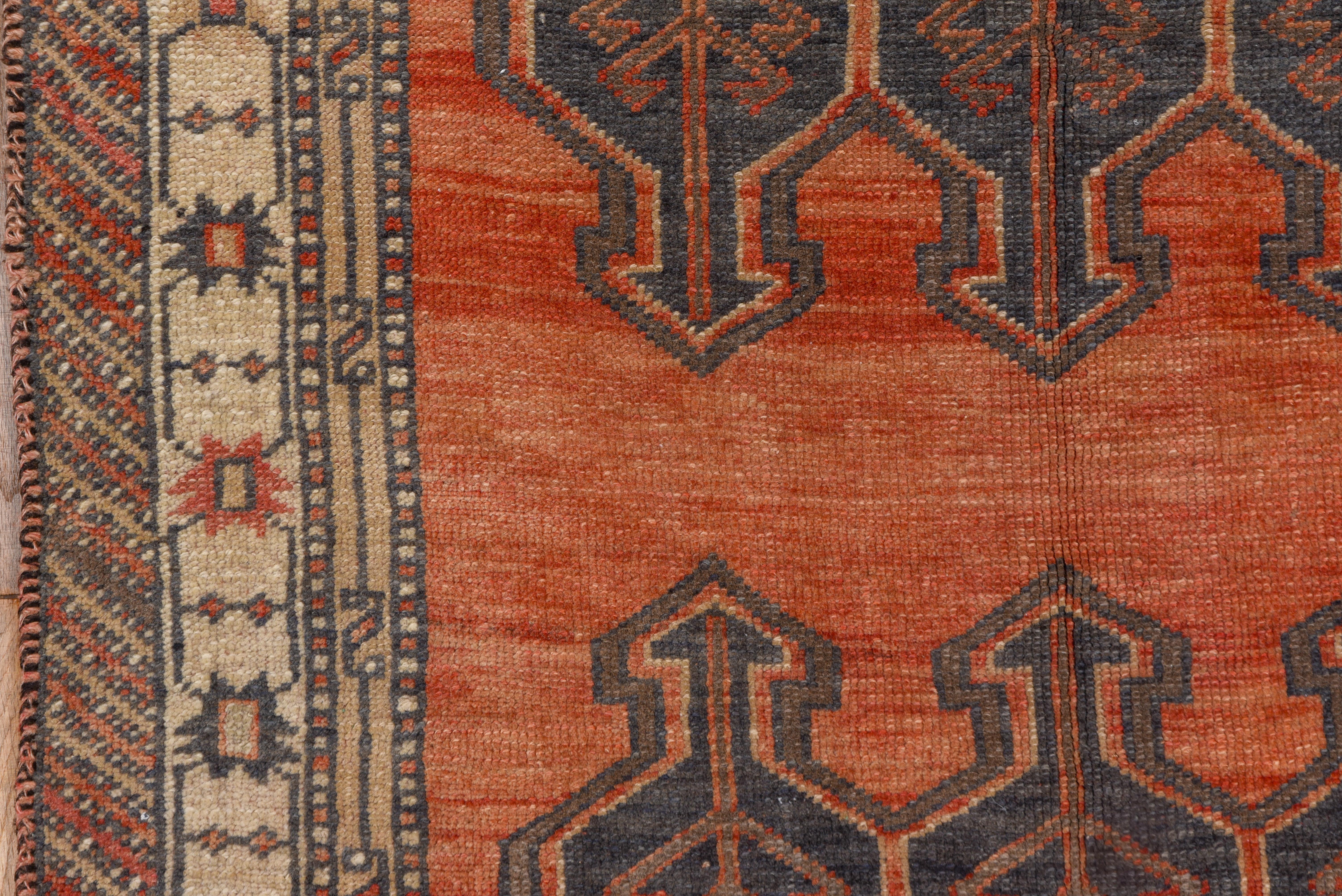 The well-abrashed soft red field of this oushak rug displays three rows each of three arrow-ended blue hexagons with interior herringbones. The ecru border shows widely separated stars.