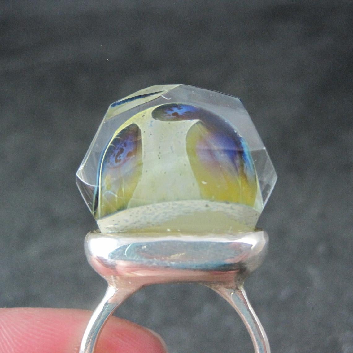 This stunning ring is sterling silver with a one-of-a-kind, high-set art glass stone.
The face of this ring measures 5/16 of an inch north to south, 13/16 of an inch east to west, and has a rise of 7/8 of an inch off the finger.
Size: 8
Marks: